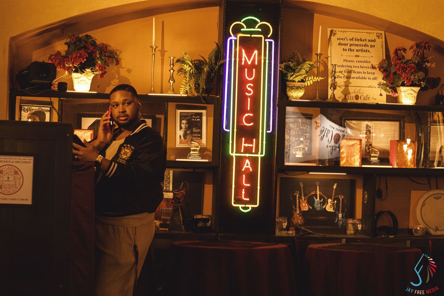 Man standing beside a glowing Music Hall neon sign in a warmly lit venue interior.