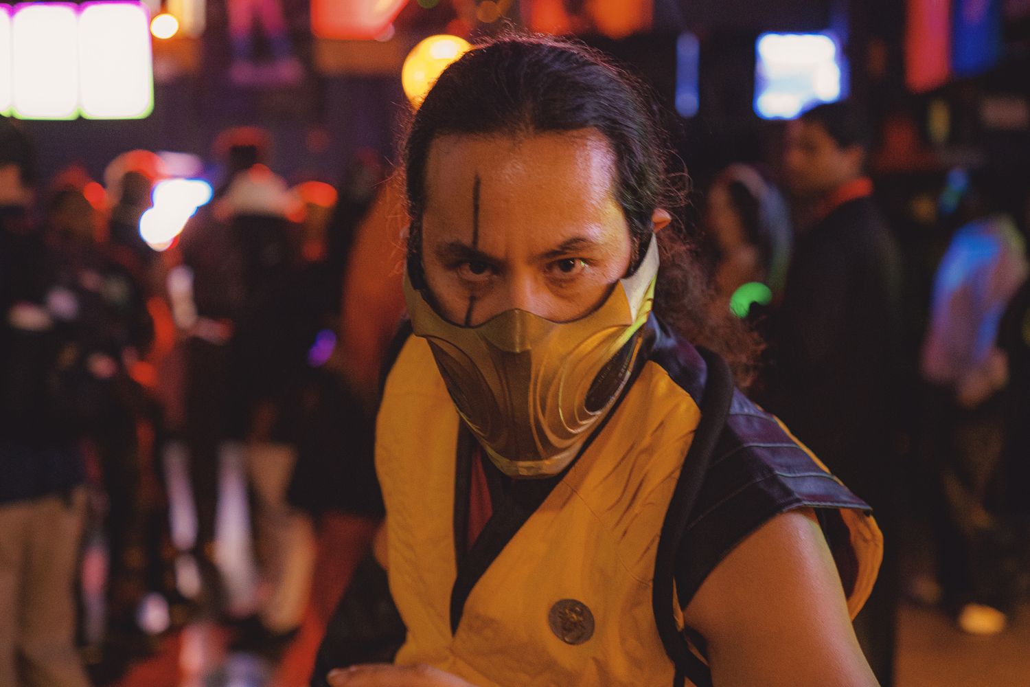 Person wearing a yellow Scorpion Mortal Kombat costume and mask at a crowded nighttime event.