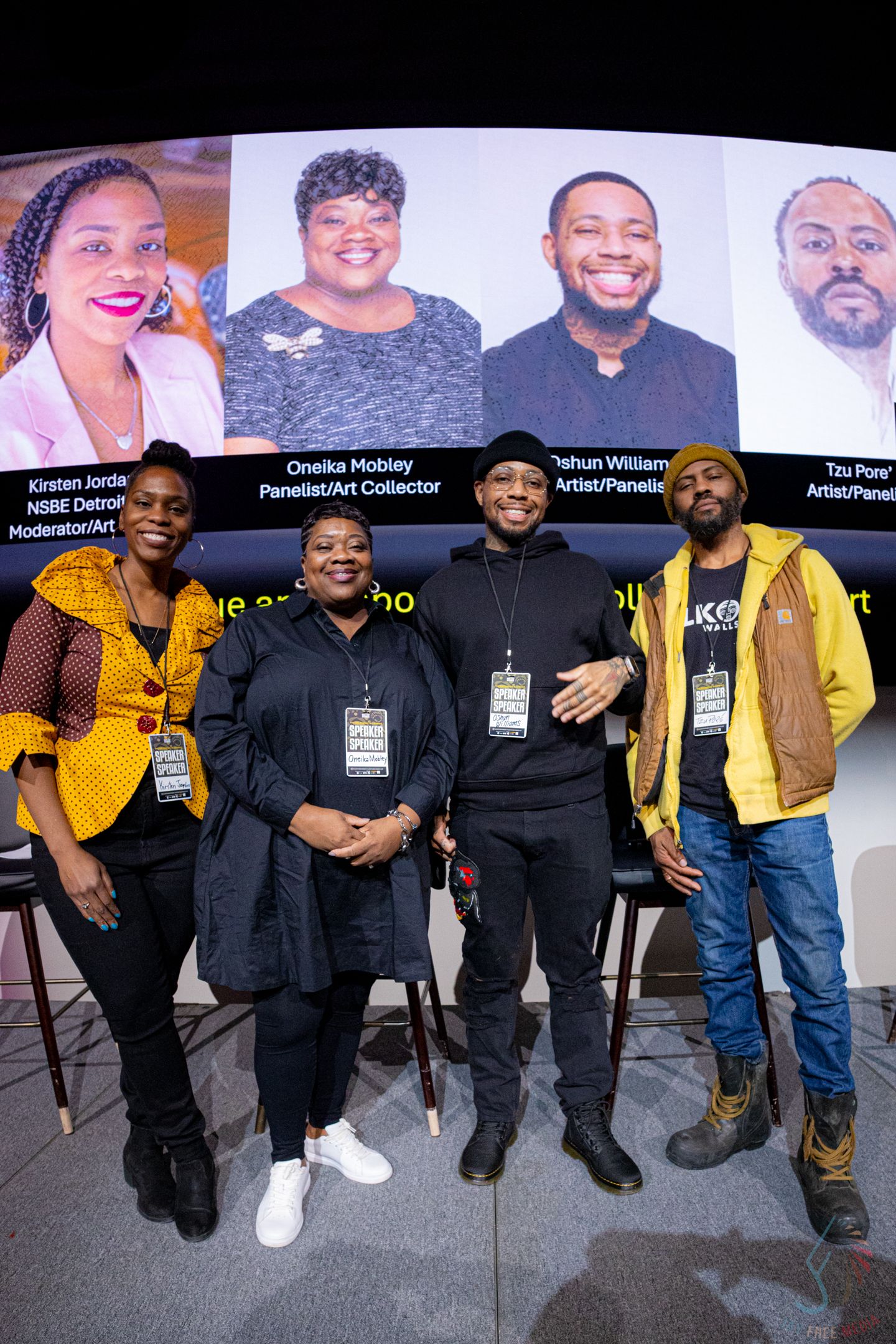 Four Black artists and panelists pose together in front of a presentation screen at a Detroit art event.