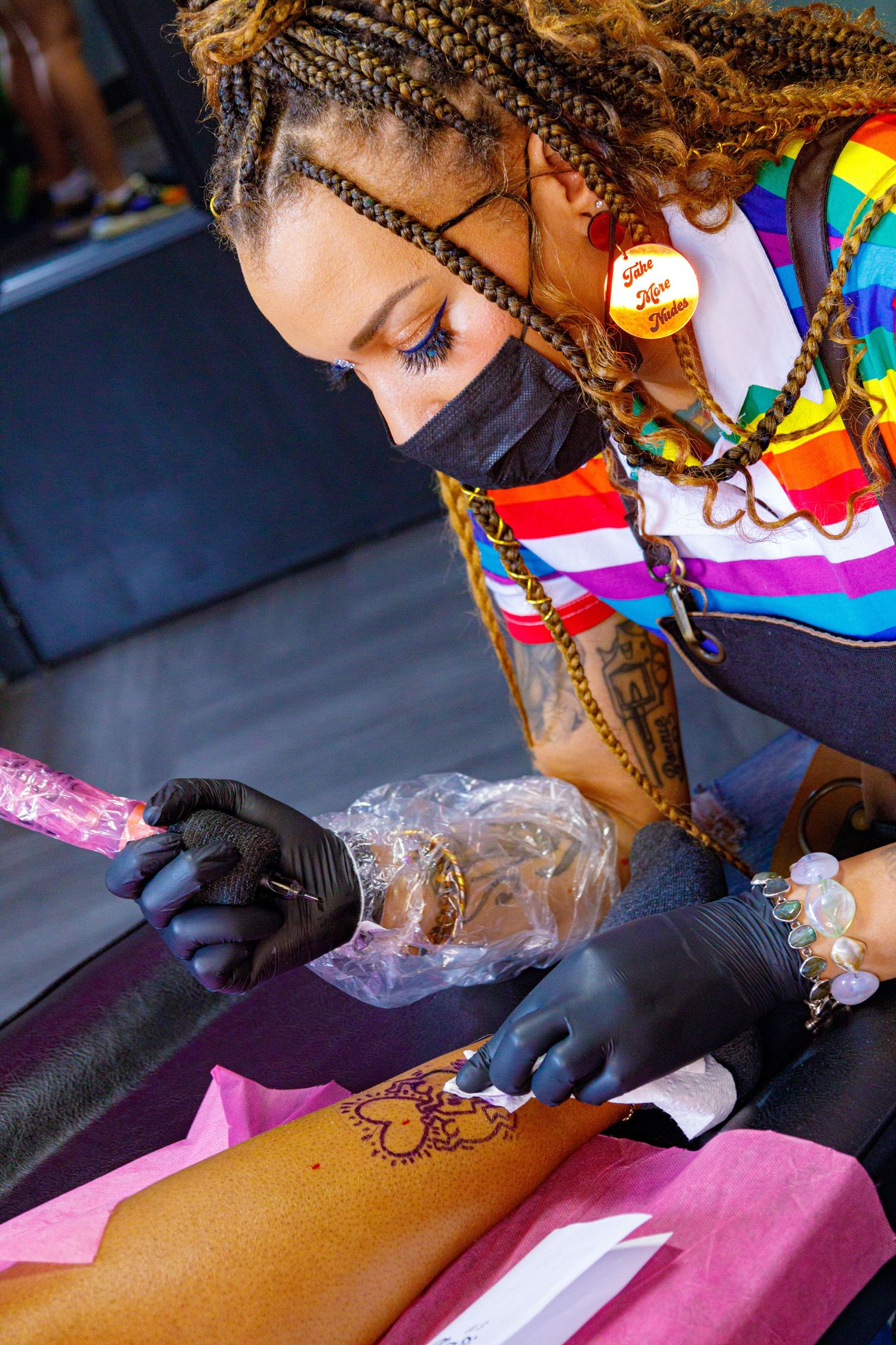Henna artist in rainbow top and black gloves applying intricate henna tattoo design on client's arm.