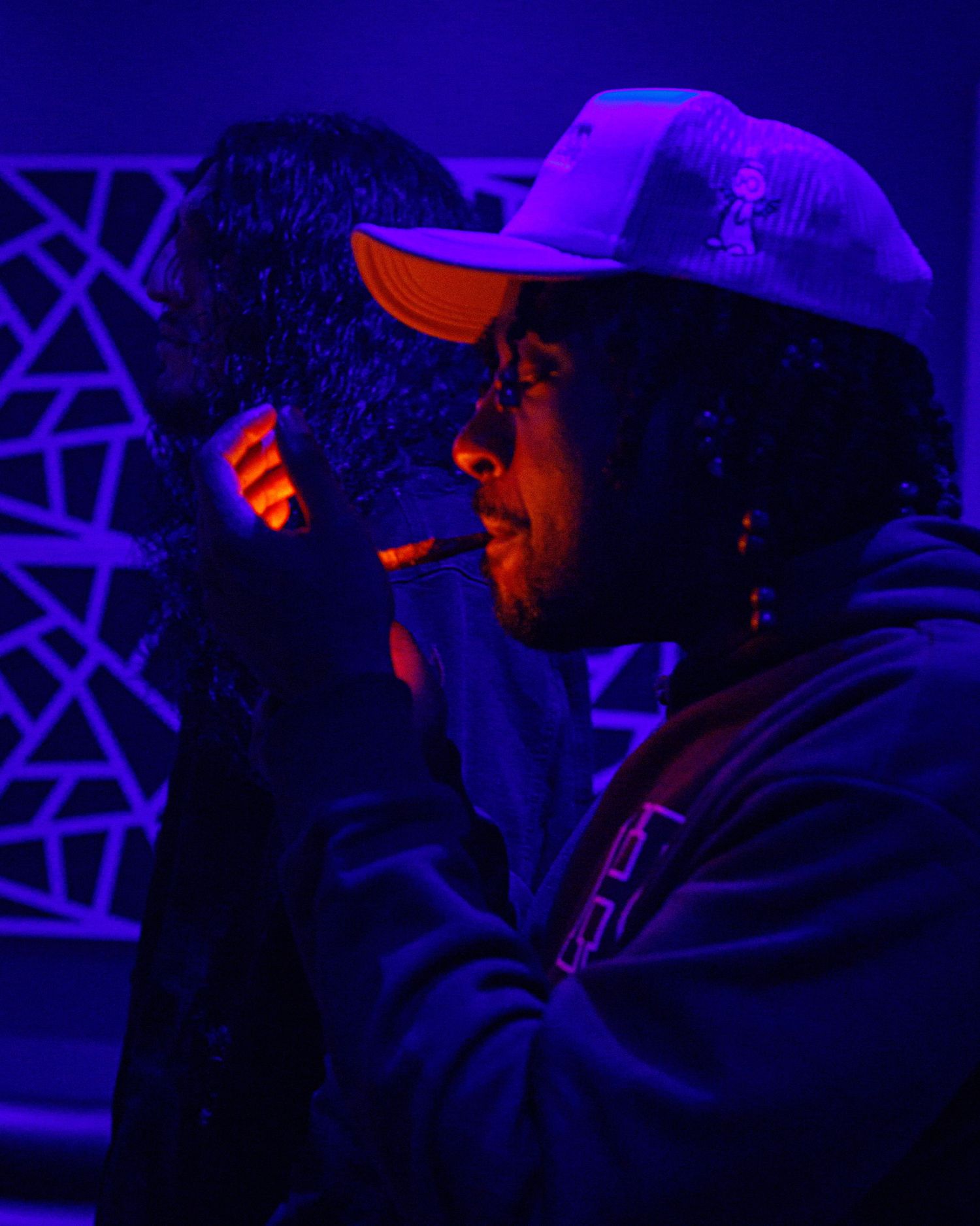 Man in white cap styling hair under blue UV lighting in dark room.