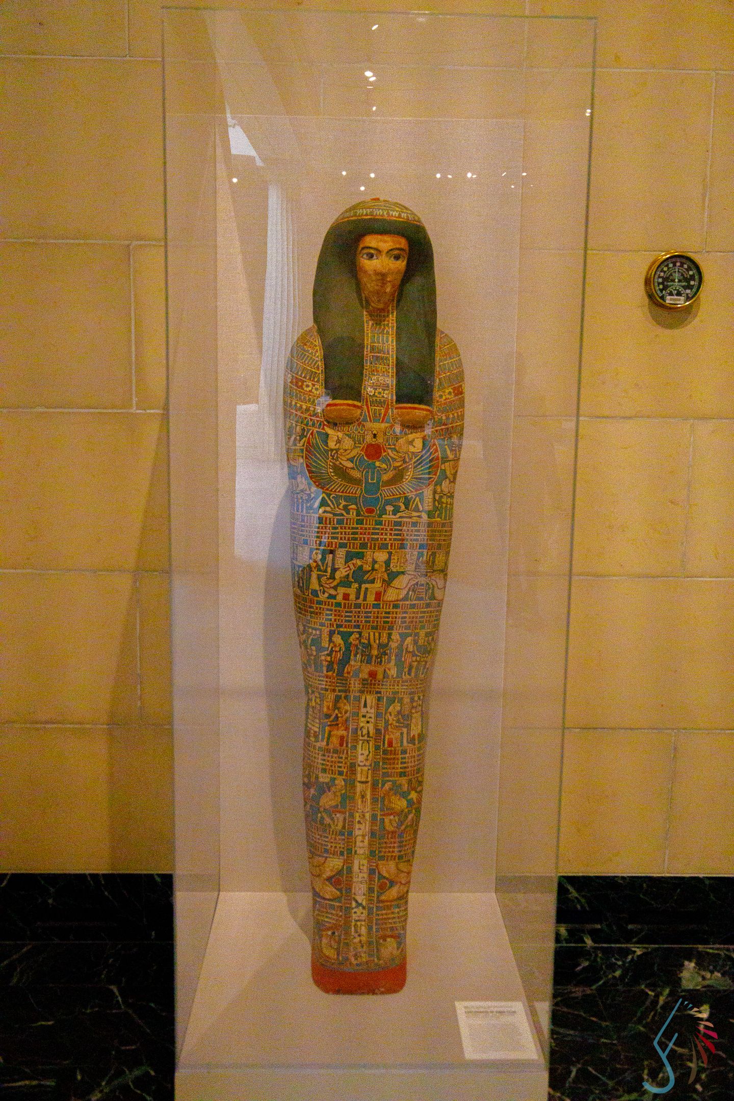 Ancient Egyptian painted wooden mummy case displayed in glass museum exhibit case.