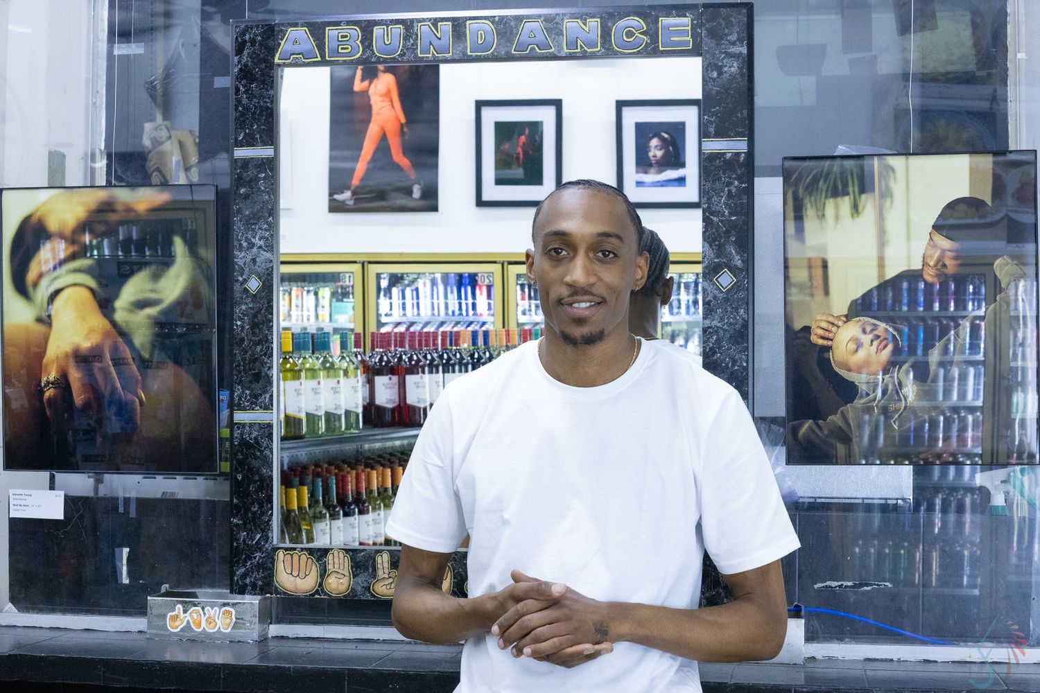 Man in white t-shirt standing in front of an Abundance store display with bottles and artwork.