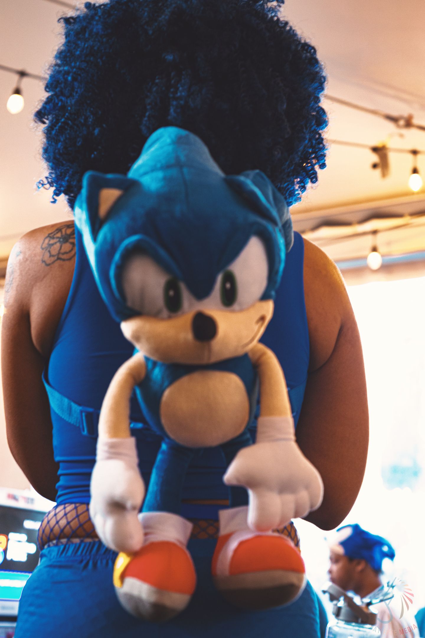 Person holding a large Sonic the Hedgehog plush toy, wearing a blue outfit with an afro hairstyle.