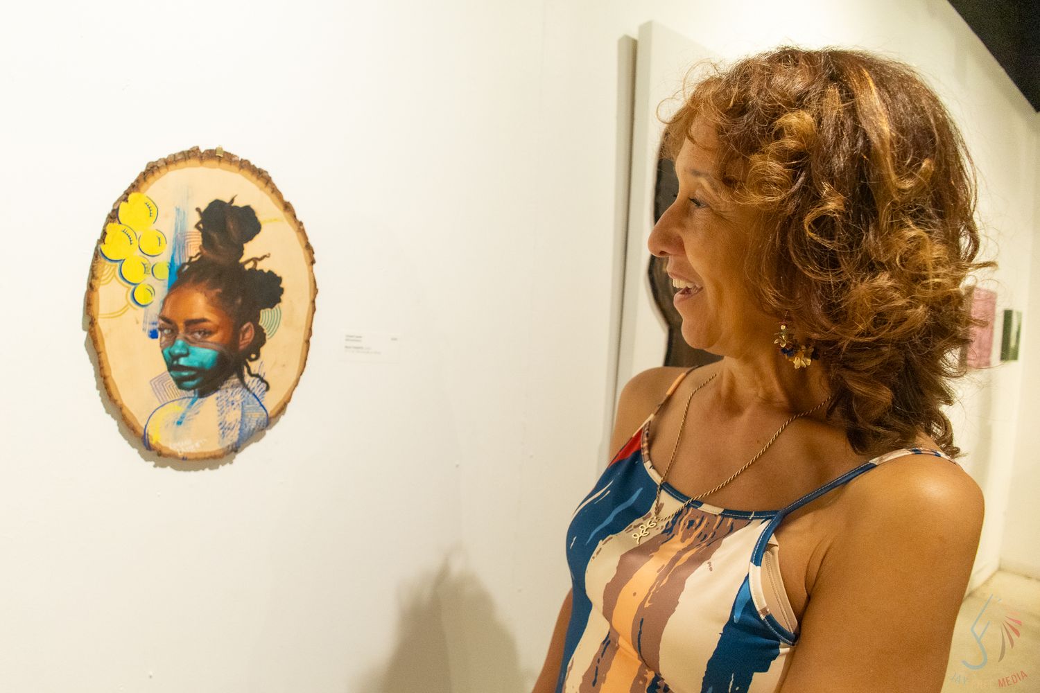 Woman with curly hair admires a portrait painting on wood slice at an art gallery.
