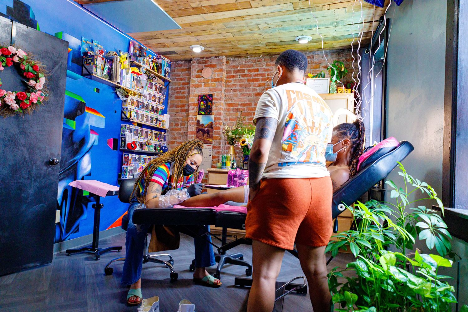 Artists and clients in a colorful tattoo studio with plants and vibrant wall art decor.