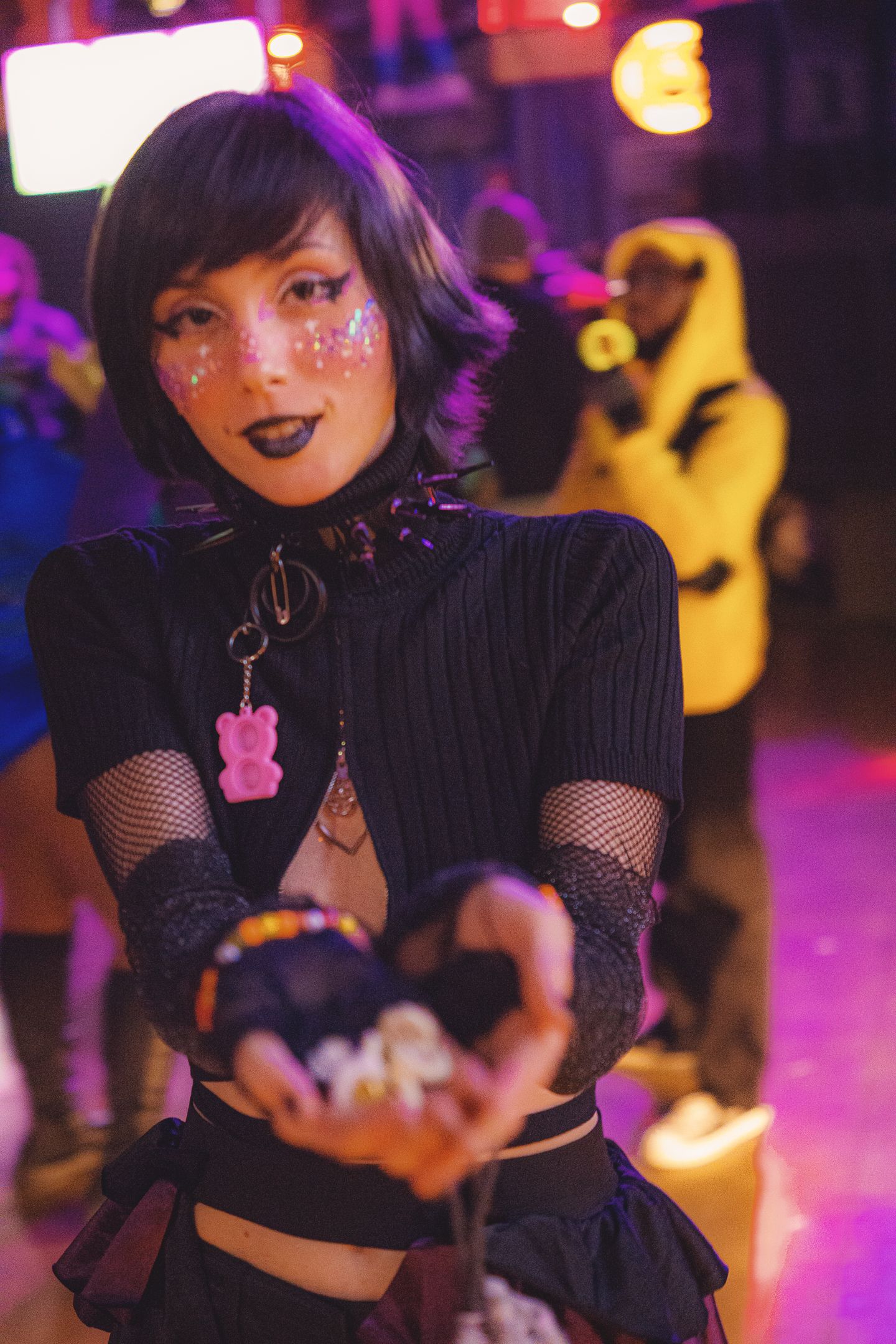 Woman in gothic costume with glitter face paint holds crystal ball at neon-lit Halloween party.