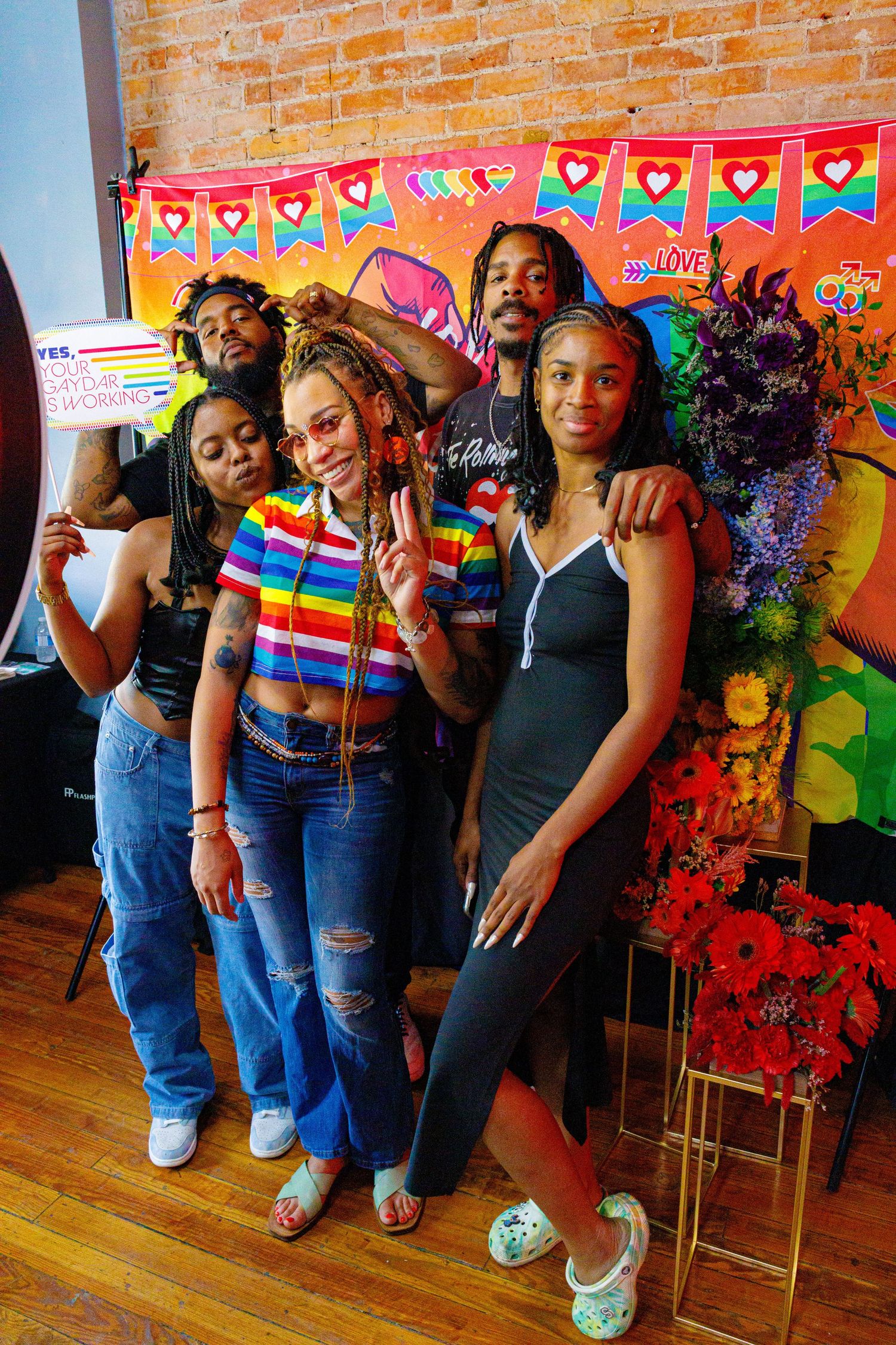 Group of friends posing together at a colorful Pride celebration event with rainbow decorations and banners.