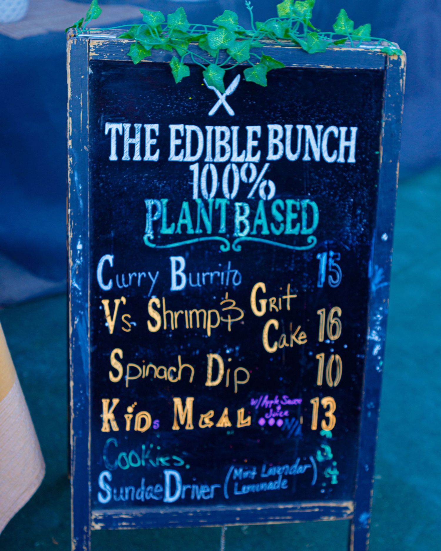 Chalkboard menu sign for The Edible Bunch, a 100% plant-based restaurant featuring curry burritos and spinach dip.