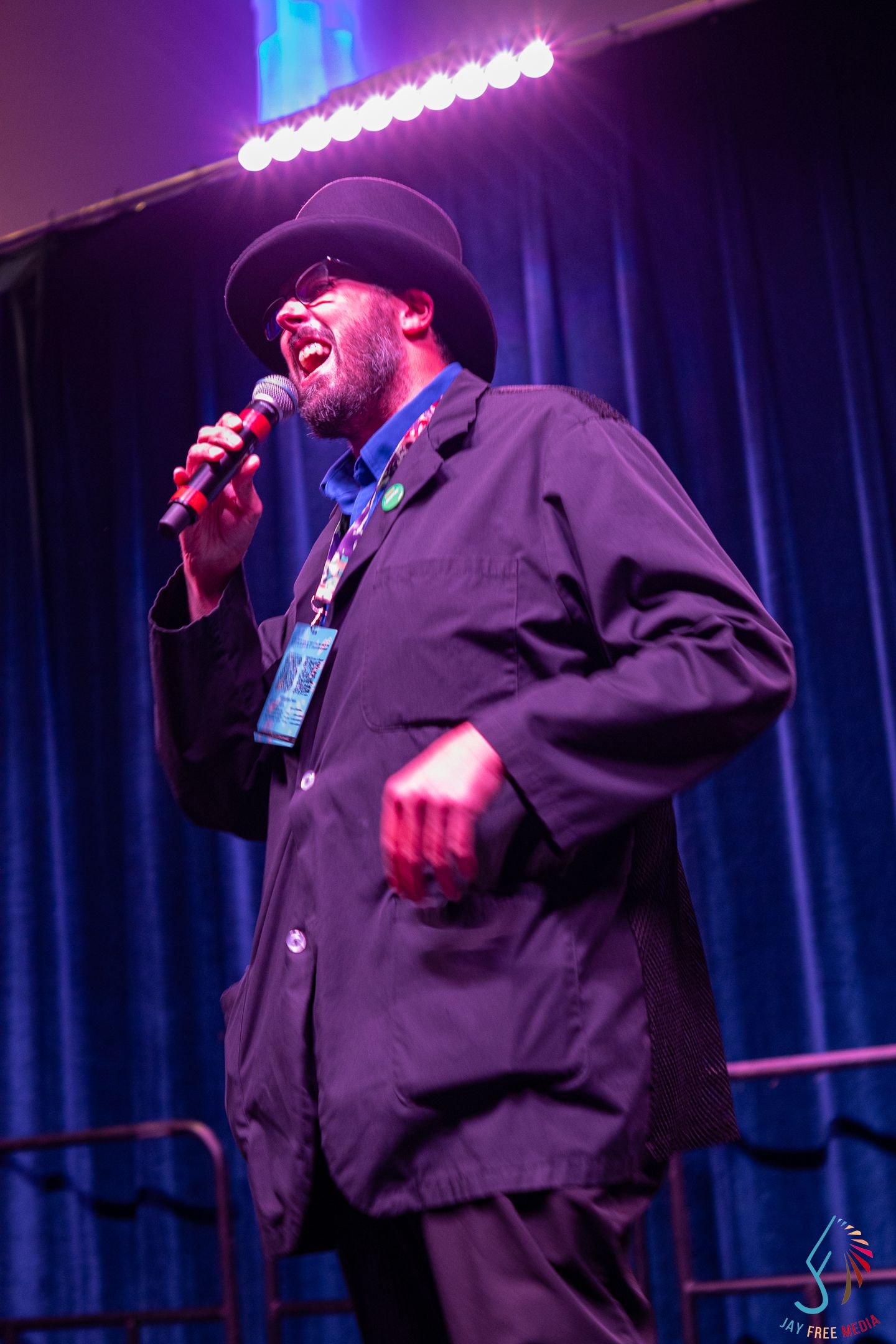 Performer in black suit and bowler hat singing into microphone on a lit stage.