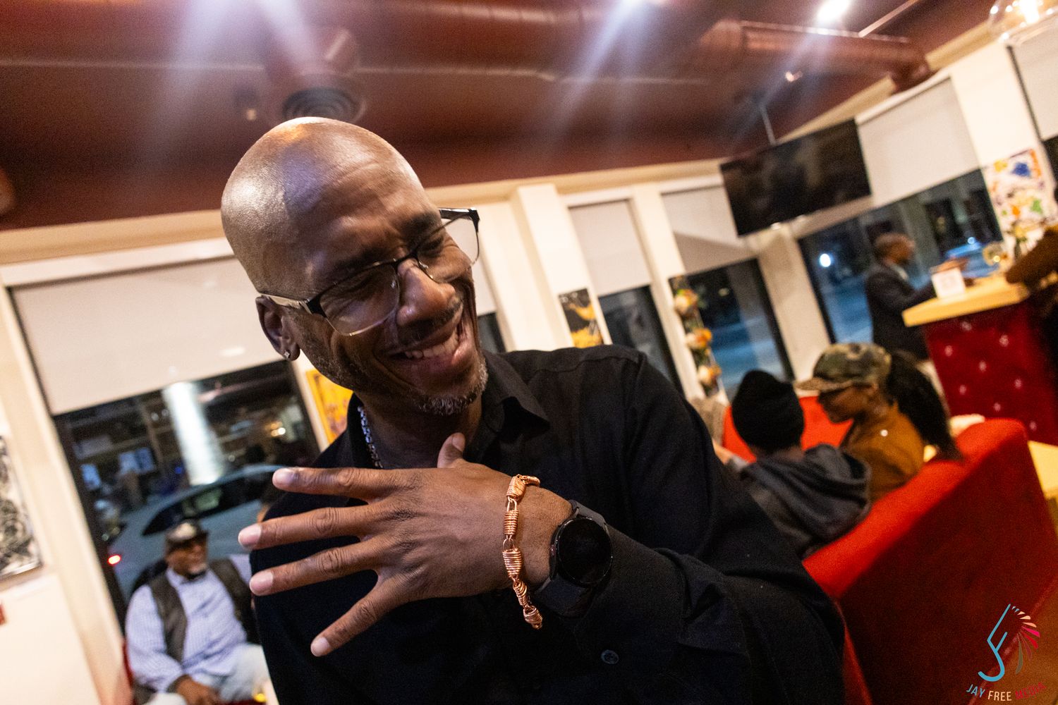Smiling man in black shirt shows his bracelet at a social gathering.