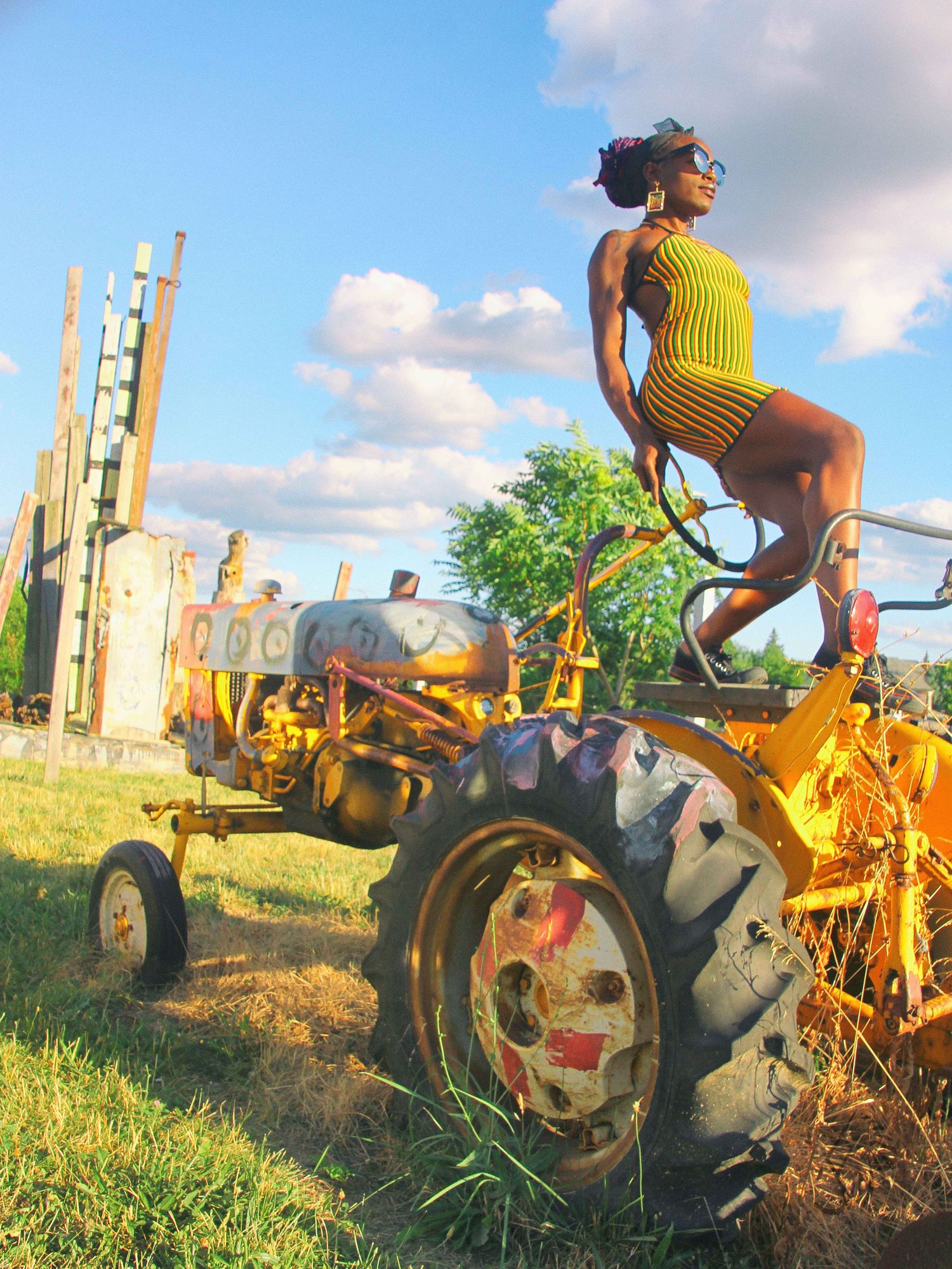 Someone in vibrant yellow clothing poses playfully on an old tractor against a blue sky.
