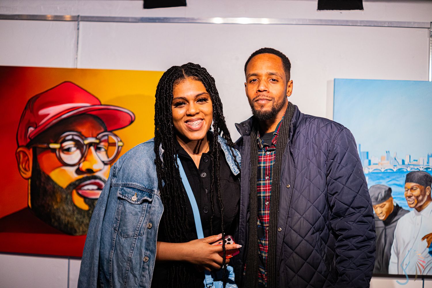 Couple posing together at an art gallery with colorful portrait paintings in the background.