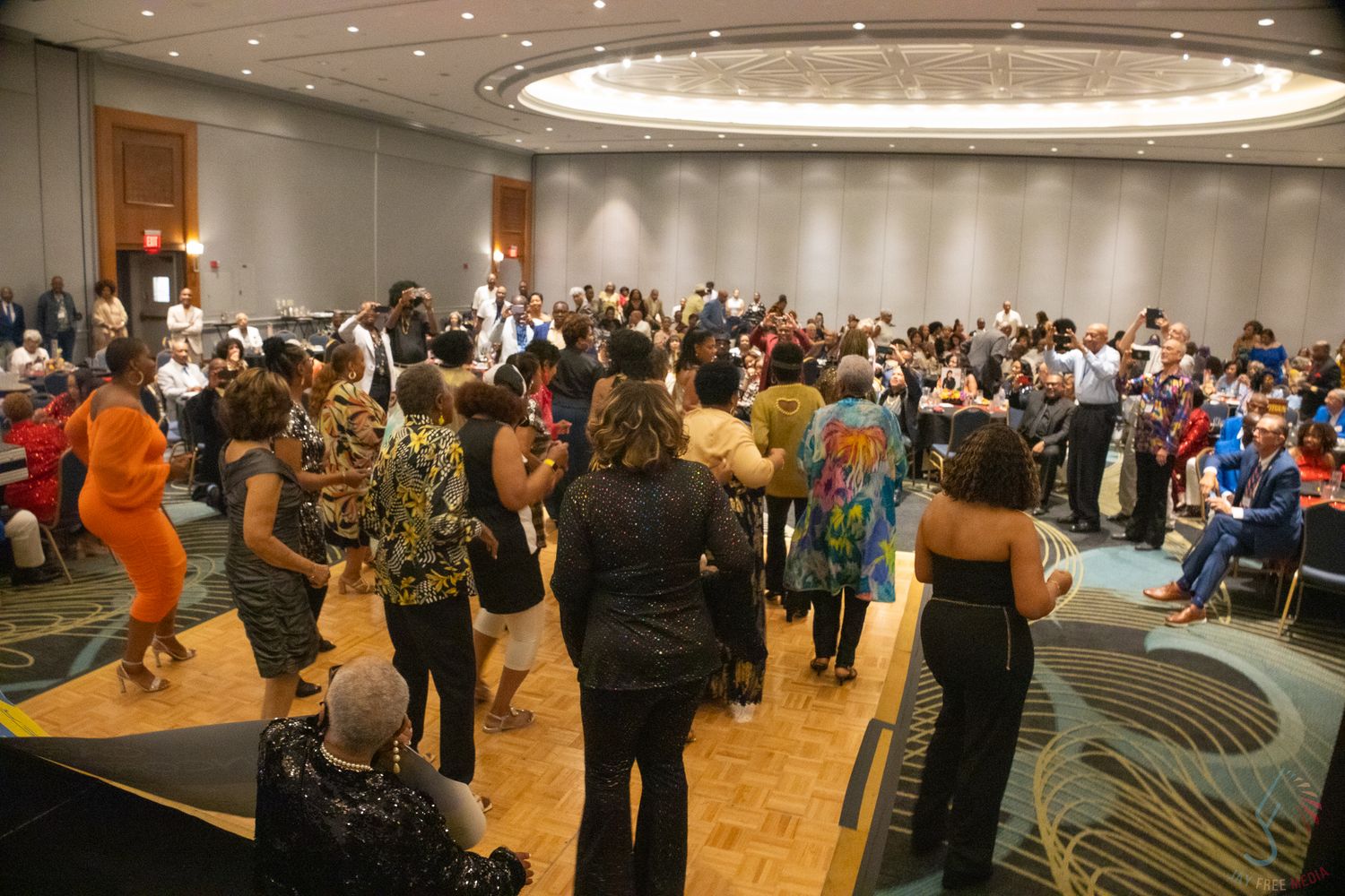 Large crowd of elegantly dressed guests dancing and mingling in a grand hotel ballroom.