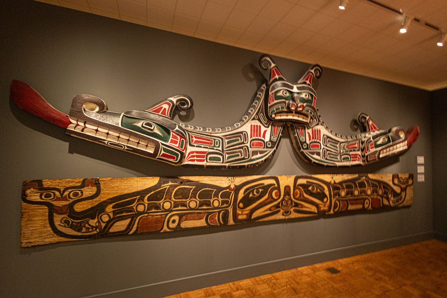 Native American totem art display featuring colorful carved wooden panels with traditional Pacific Northwest Indigenous designs in a museum.