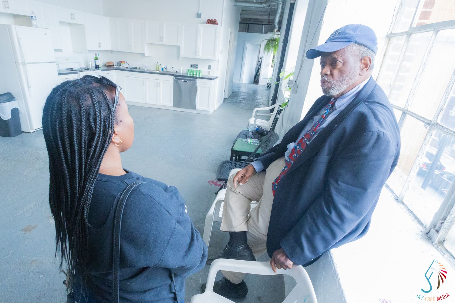 Two people engaged in conversation in a modern indoor space, one wearing a blue cap and blazer.
