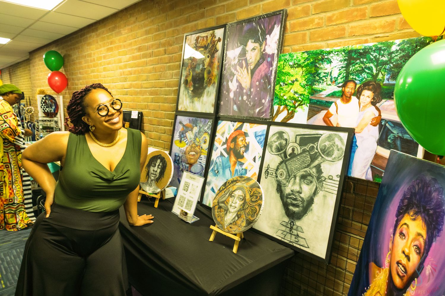 Woman poses beside colorful artwork display featuring portraits and photos at an art exhibition with festive balloons.