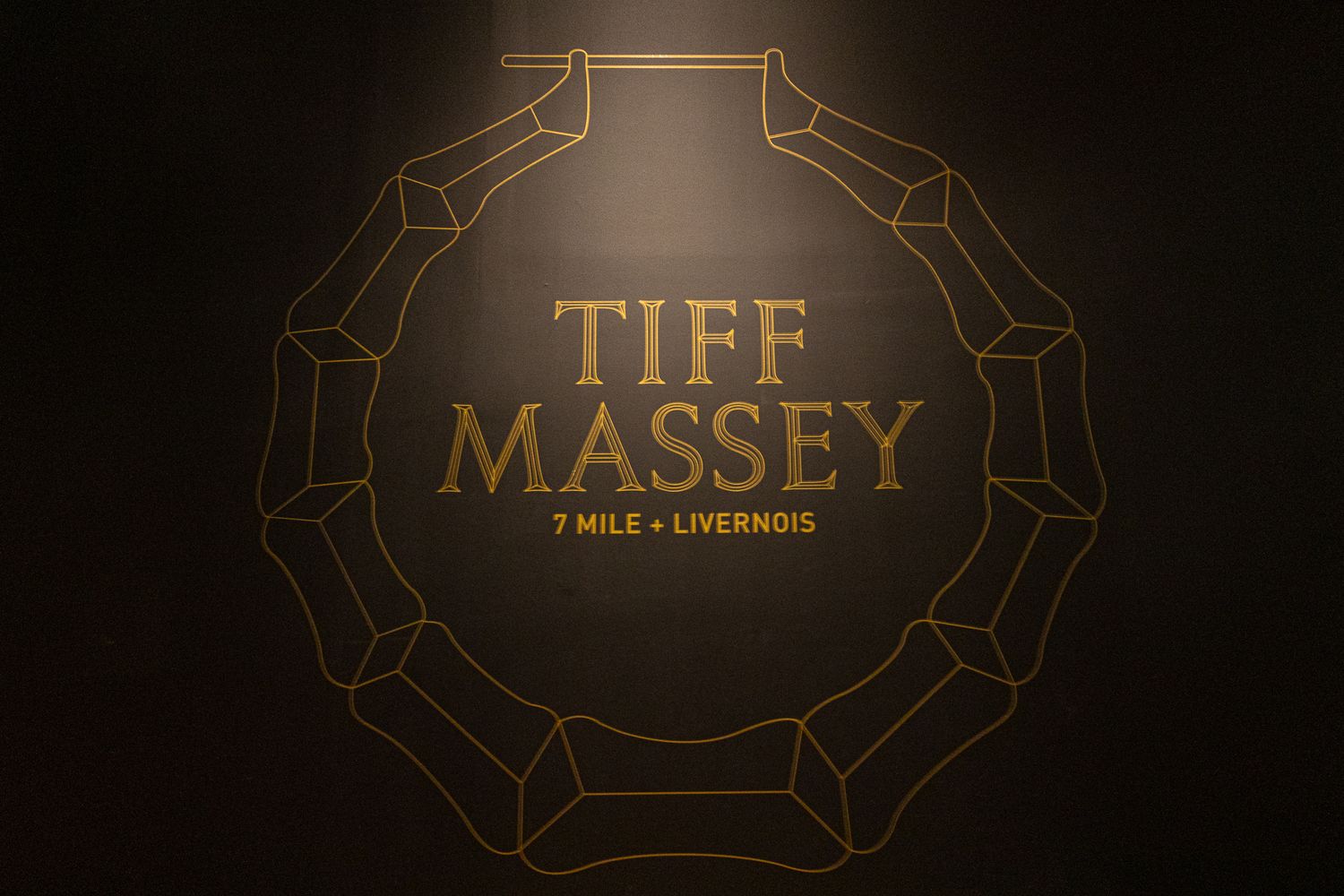 Tiff Massey 7 Mile Livernois gold logo on dark background at art exhibition.