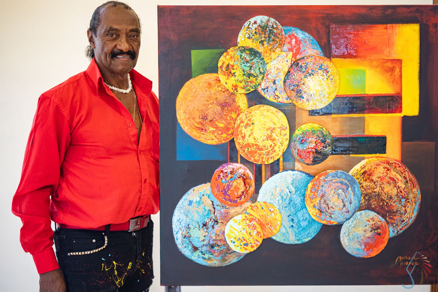 Man in red shirt standing beside colorful abstract painting with spheres on canvas in art gallery.