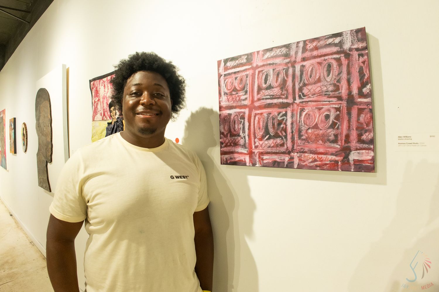 Young man smiling in art gallery beside vibrant red abstract painting on white wall.