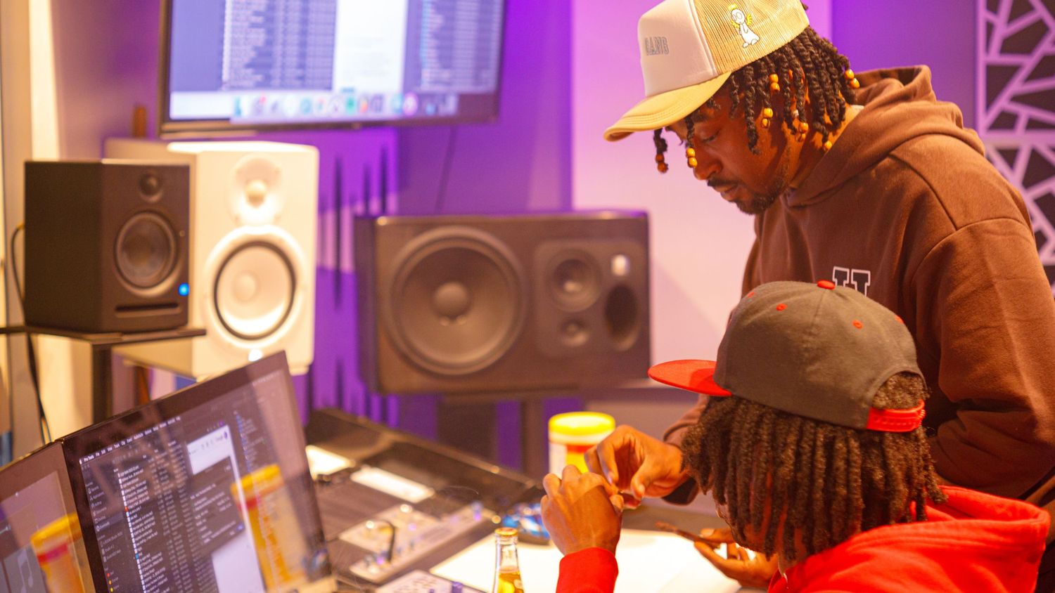 Two musicians collaborating in a professional recording studio with monitors and mixing equipment.