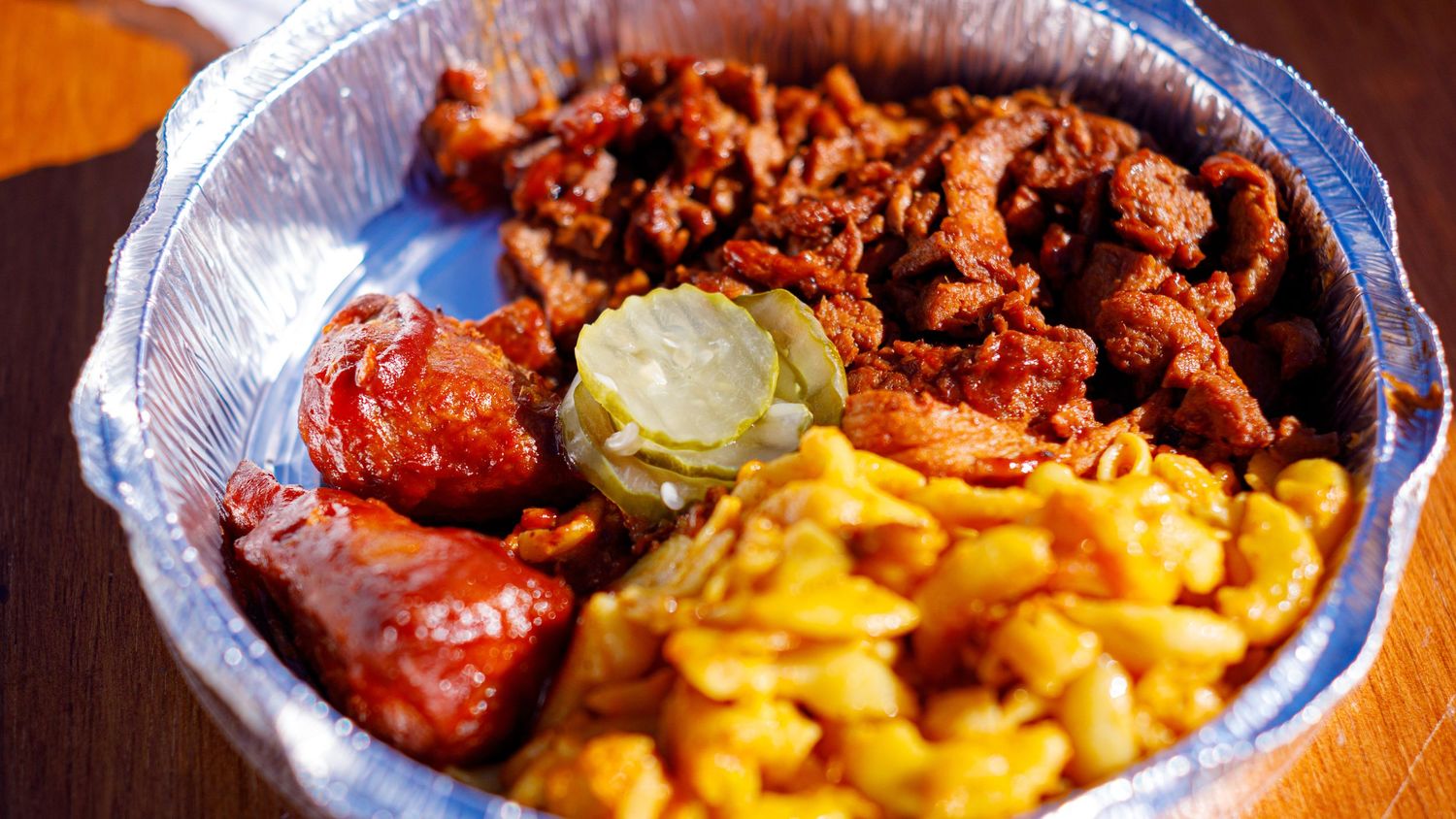 BBQ plate with pulled pork, fried chicken, sausage, pickles, and macaroni and cheese in foil tray.