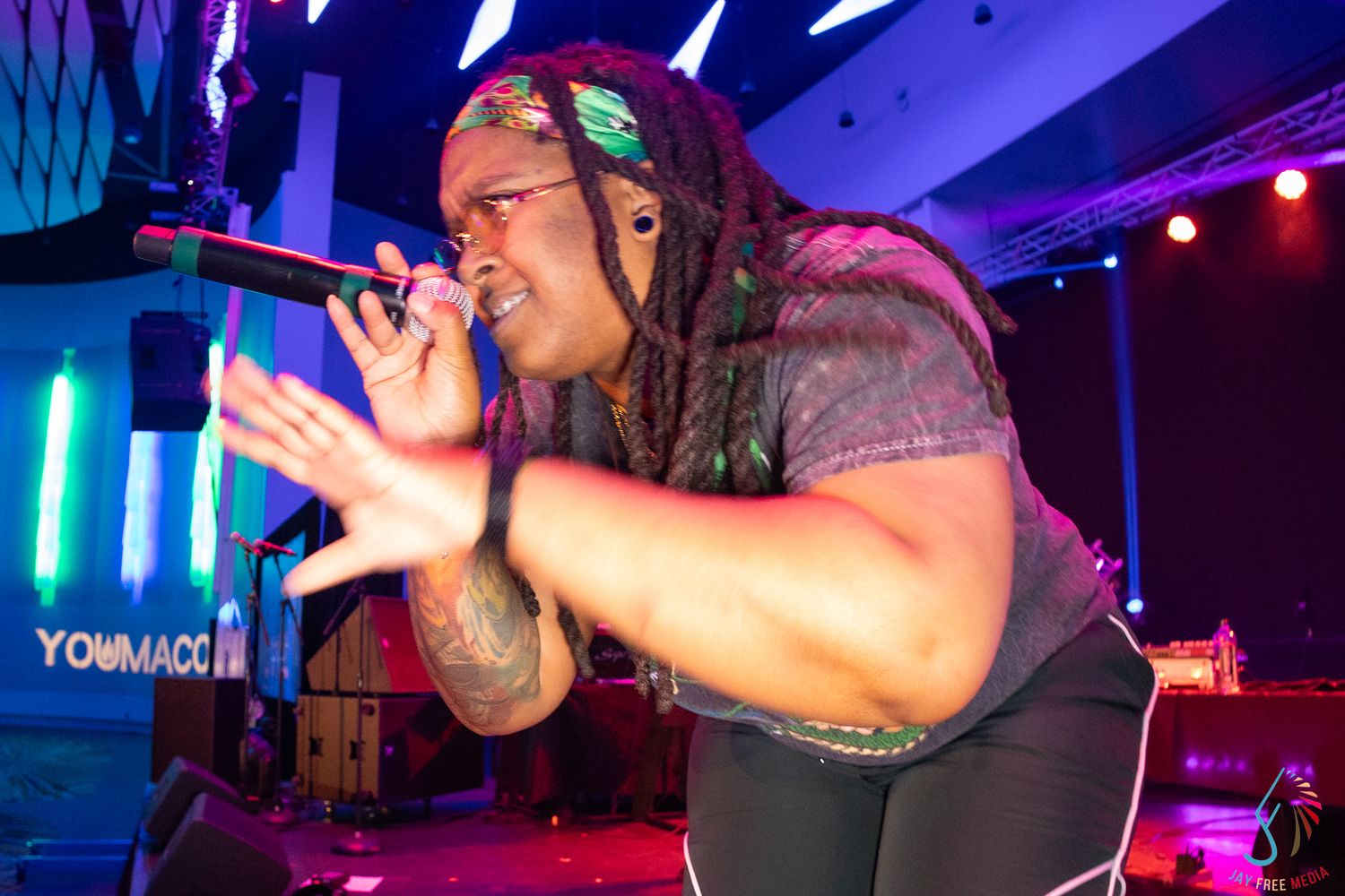 Energetic performer singing passionately into microphone under colorful stage lights at convention.