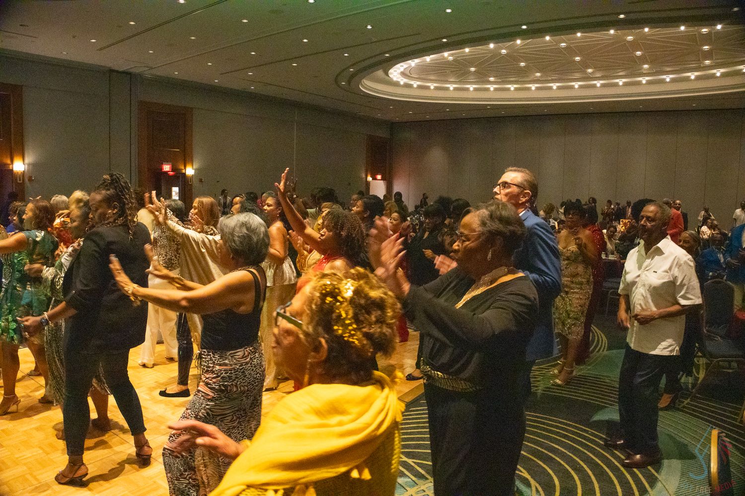 Diverse crowd of guests dancing and celebrating together in a ballroom event.