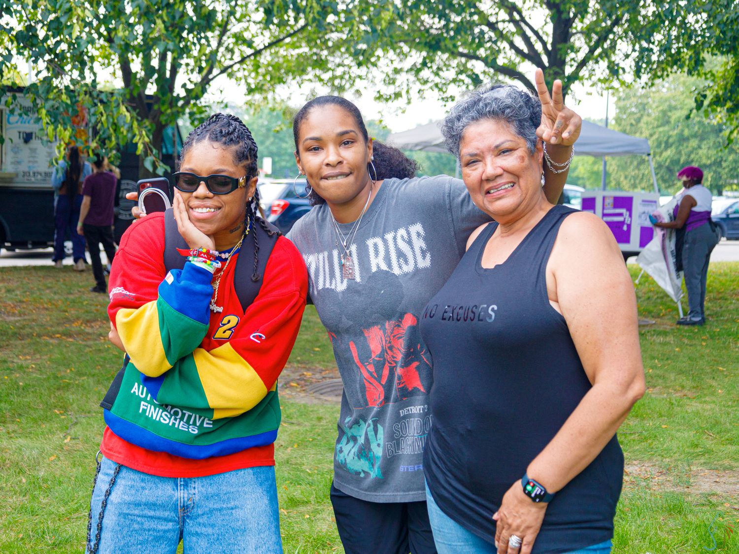 Three women smiling and posing together at an outdoor community event in a park.