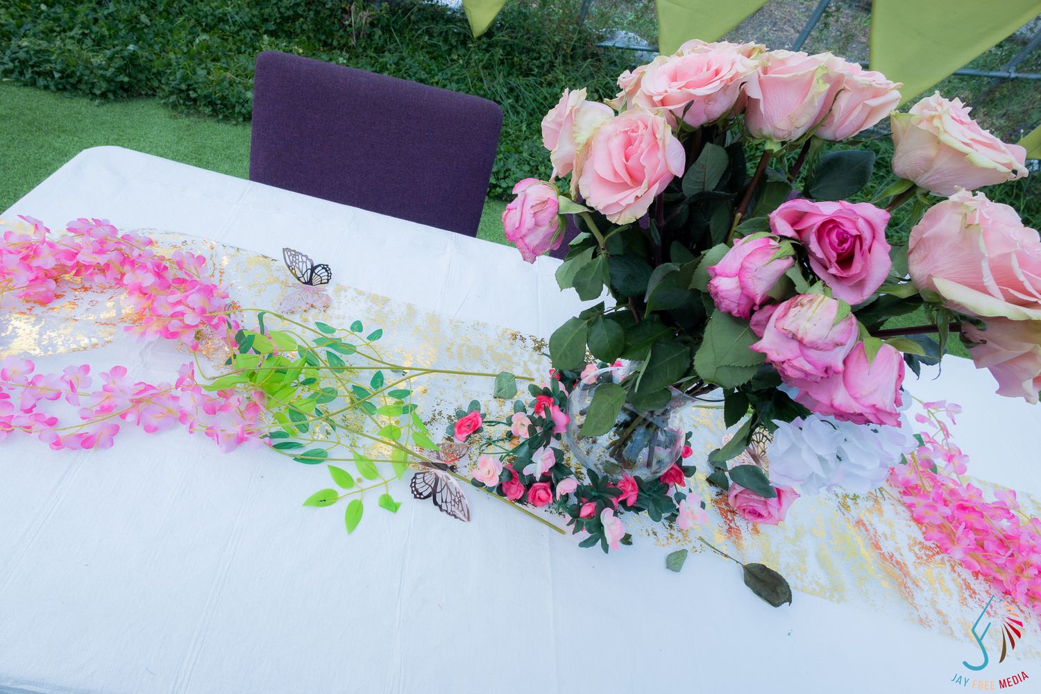 Pink roses and floral garland decorating a white table at an elegant outdoor event or wedding reception.