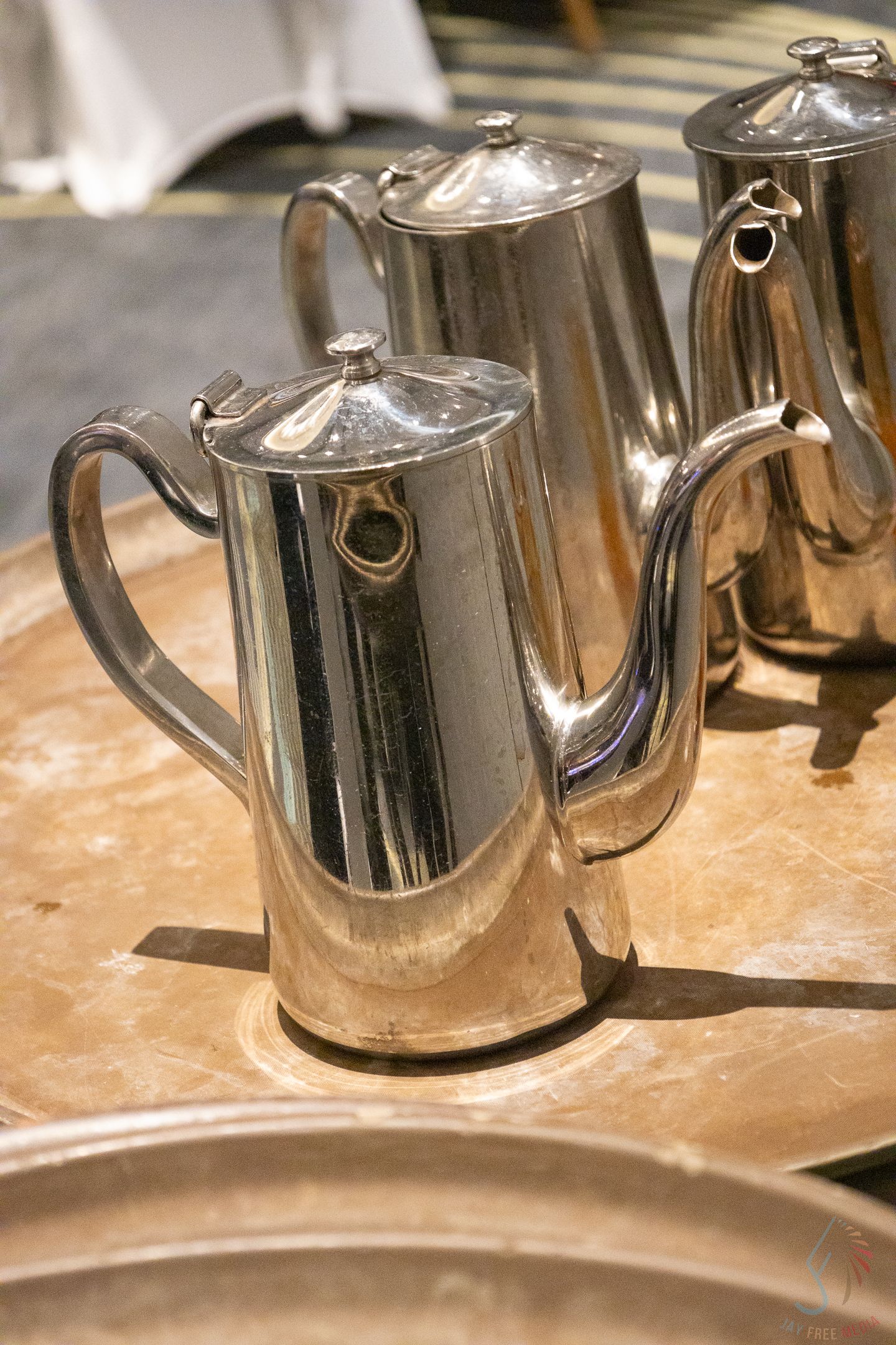 Polished silver teapots on a wooden tray at a formal catering event.