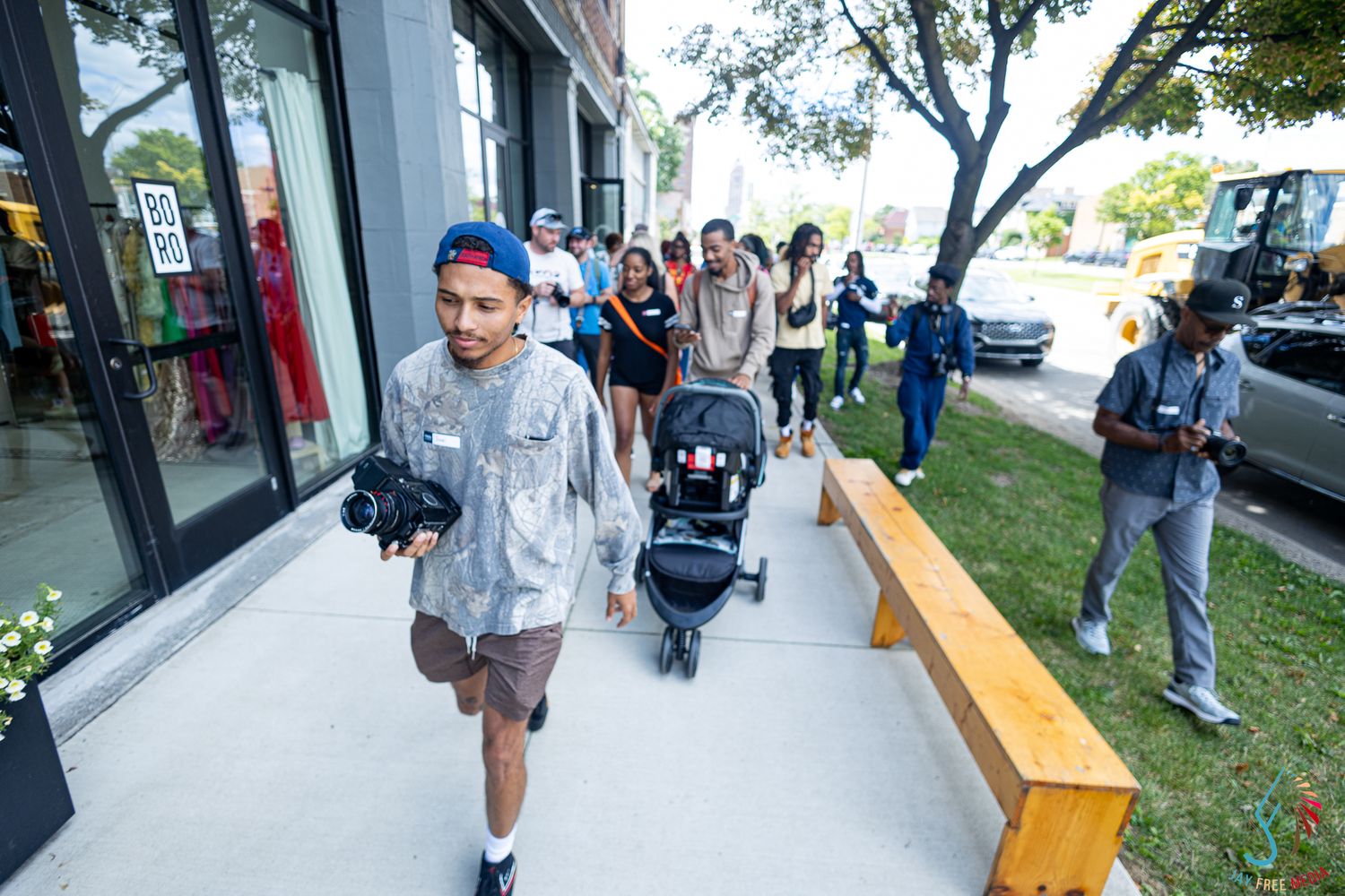 Group of people walking along a sunny urban sidewalk outside a modern storefront.