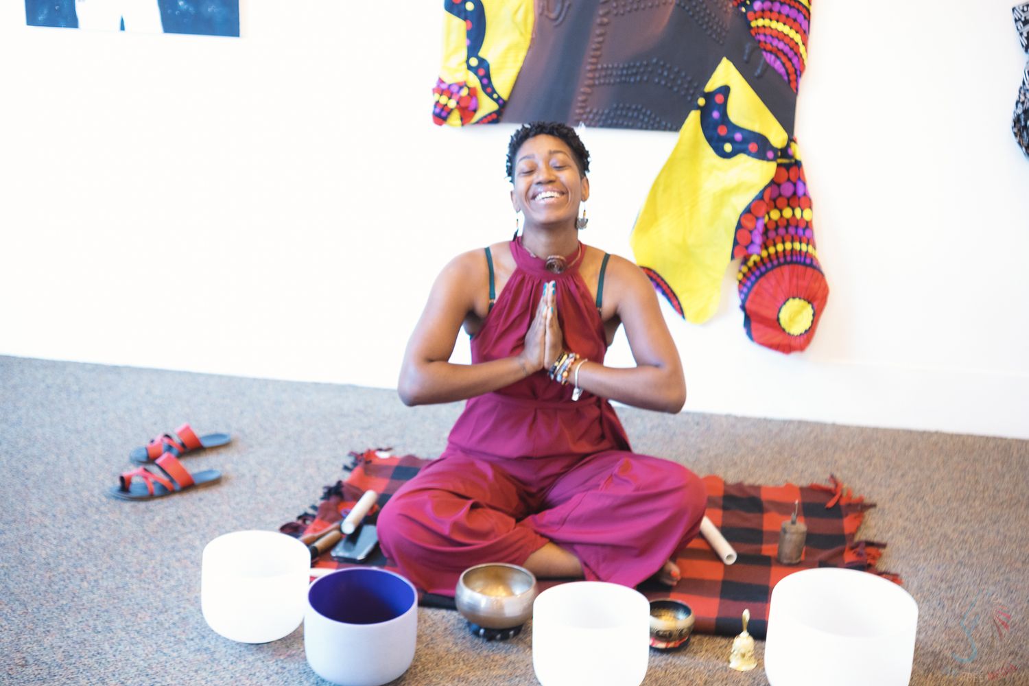 Woman meditating in lotus pose with singing bowls on colorful mat in yoga studio.