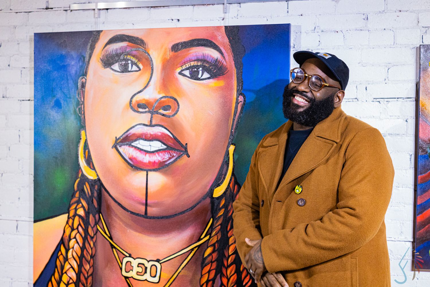 Man smiling proudly beside a large colorful portrait painting of a woman at an art gallery.