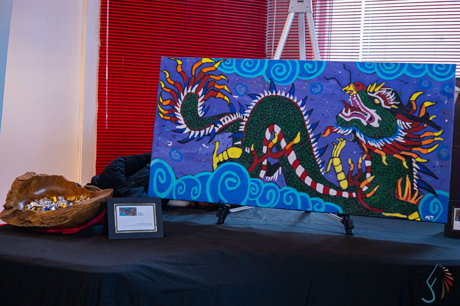 Colorful painting of a green dragon on a purple background displayed on an easel at an art exhibition.