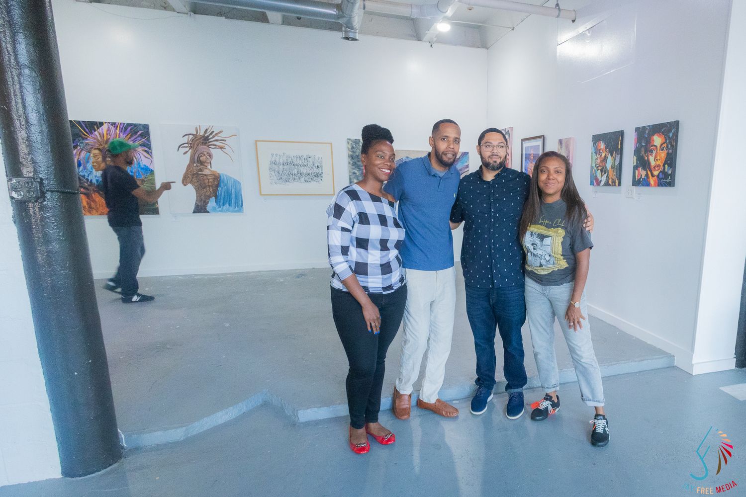 Four people pose together smiling in a modern art gallery with colorful paintings displayed on white walls.