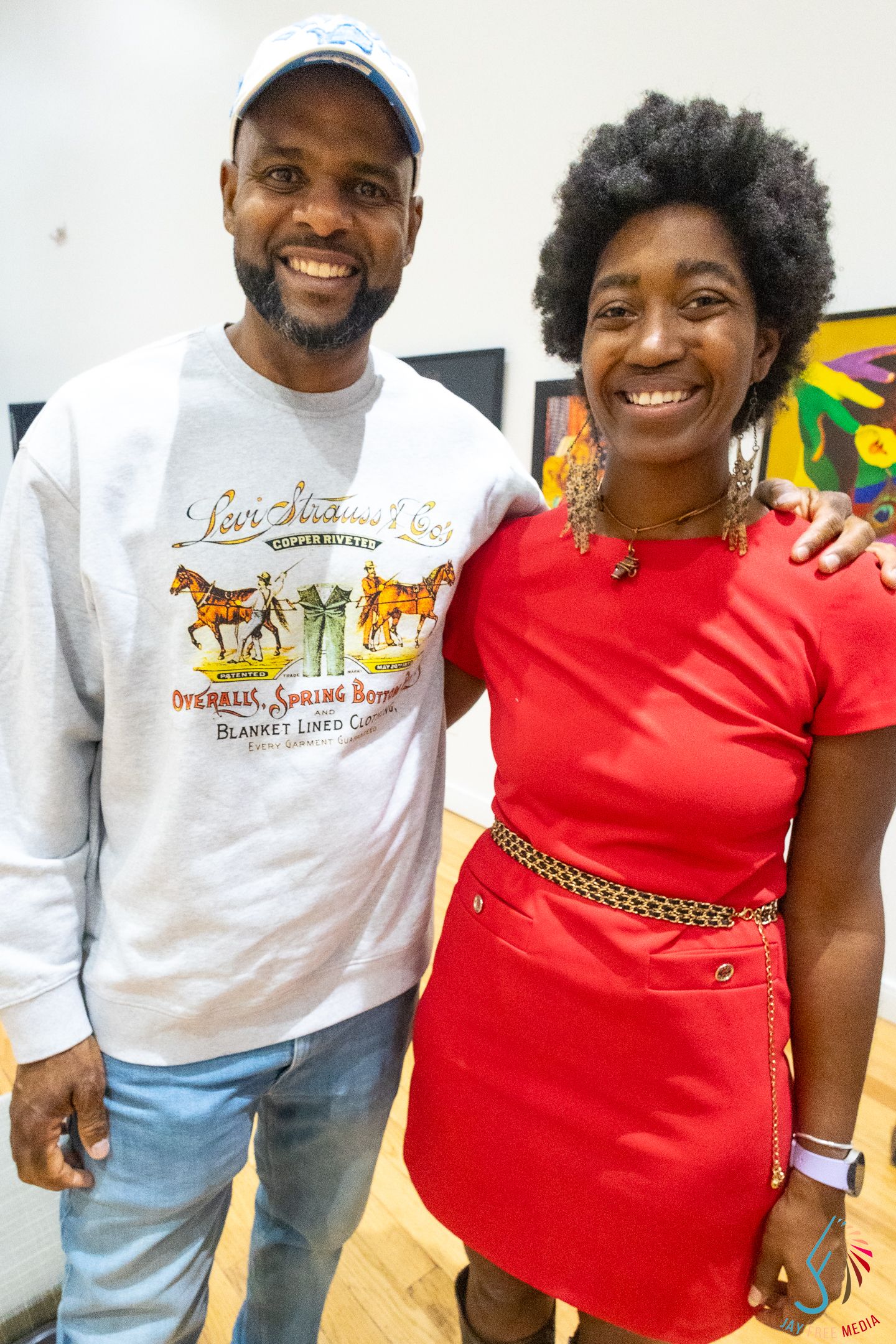 Two smiling people pose together, man in Levi Strauss sweatshirt and woman in red dress with gold belt.