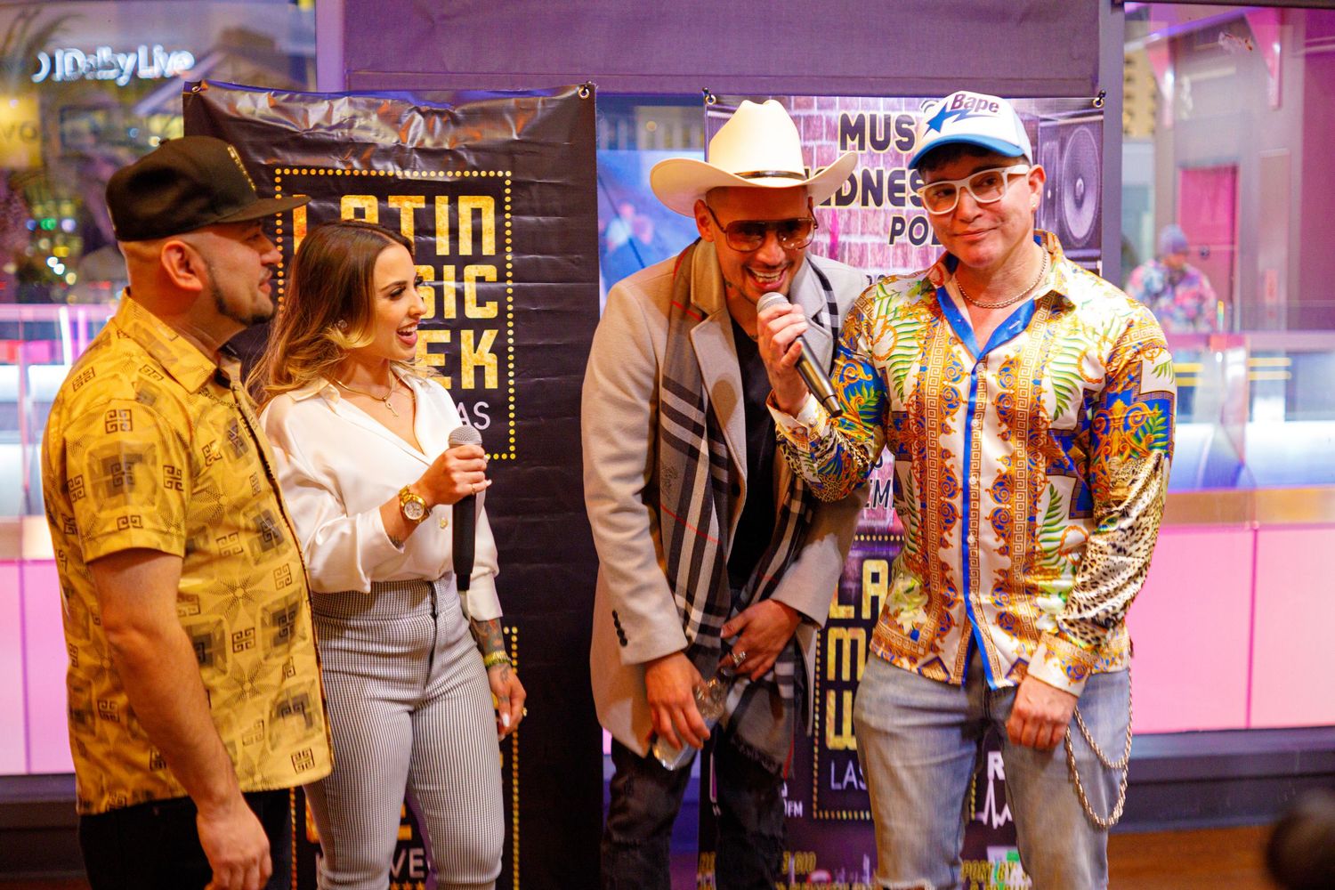 Four people laughing and talking with microphone at Latin Music Week Las Vegas event.