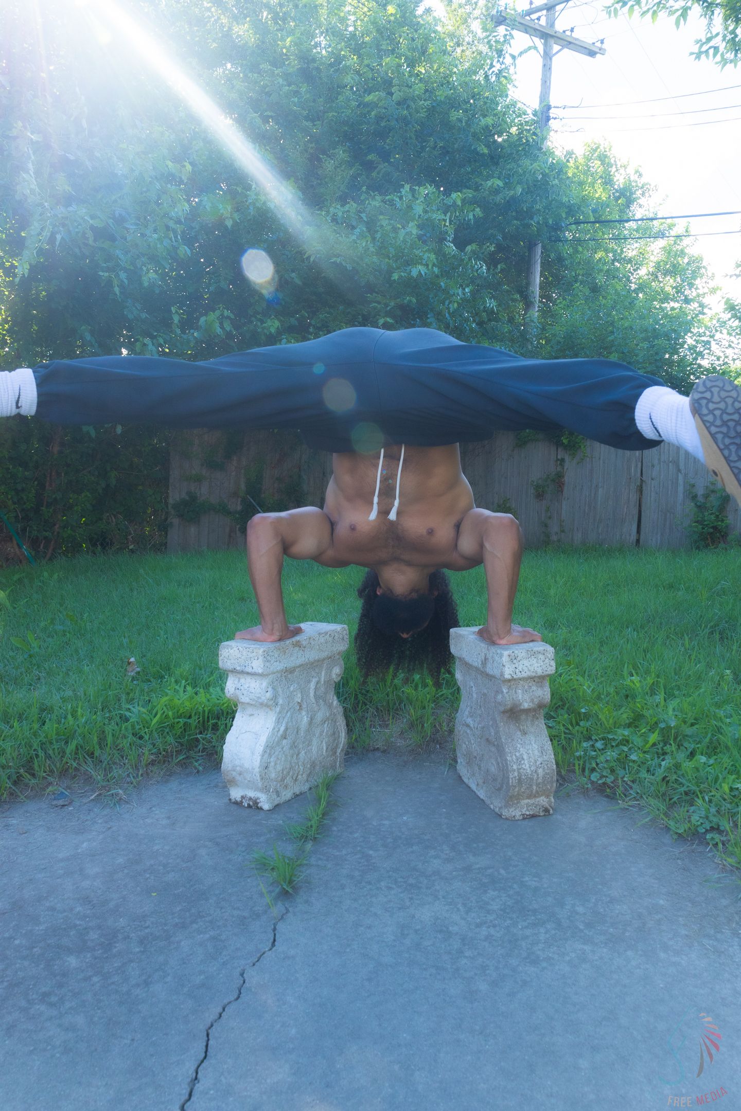 Person performing a headstand on stone pedestals outdoors, displaying impressive balance and strength in a backyard setting.
