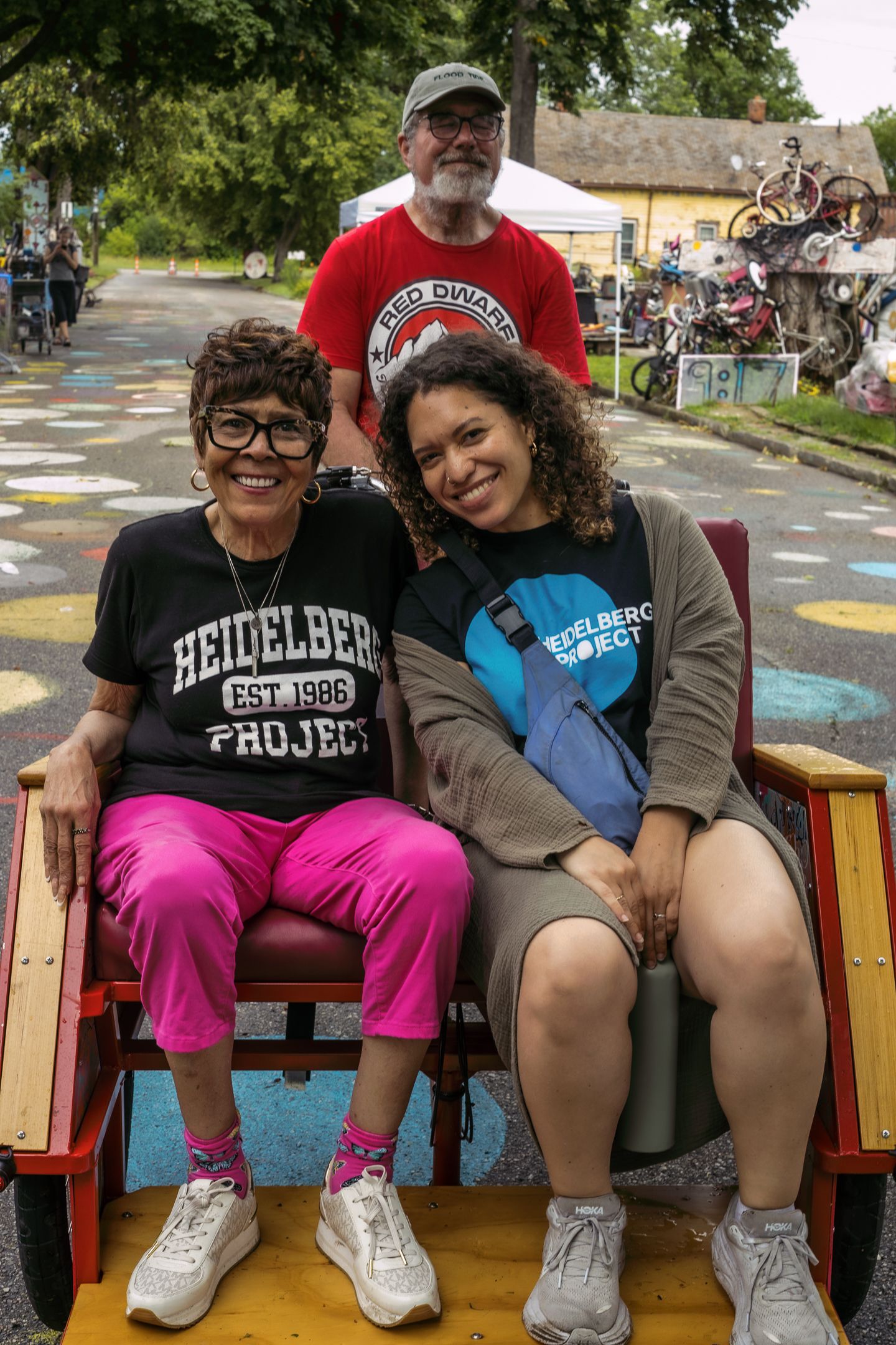 Two women wearing Heidelberg Project shirts sit in a cart at the colorful Heidelberg Project art installation in Detroit.