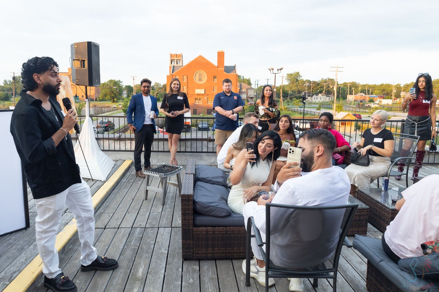 Speaker addresses diverse group of attendees at rooftop outdoor networking event.