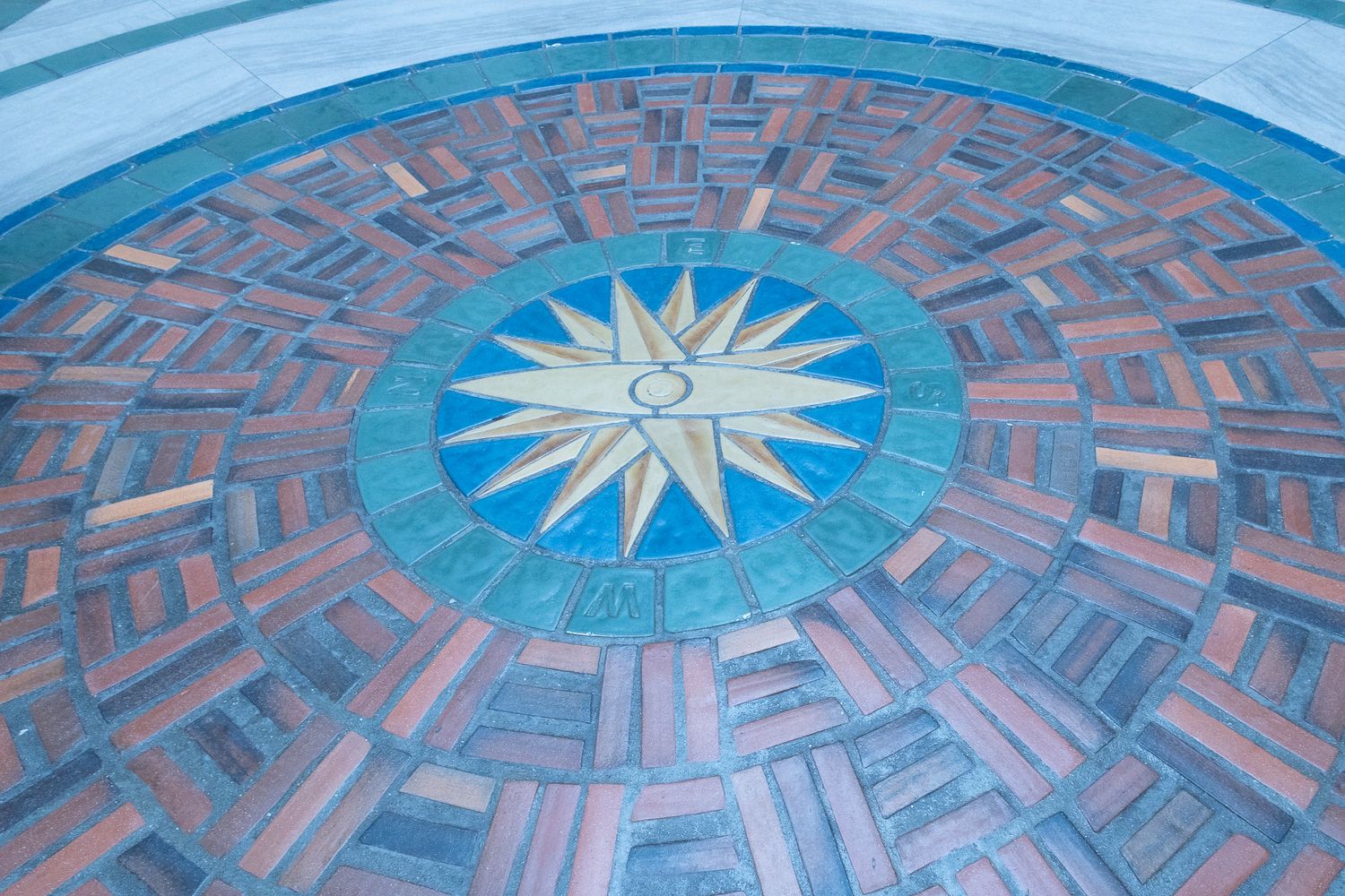 Ornate circular mosaic floor featuring a compass rose design in blue and copper tones.