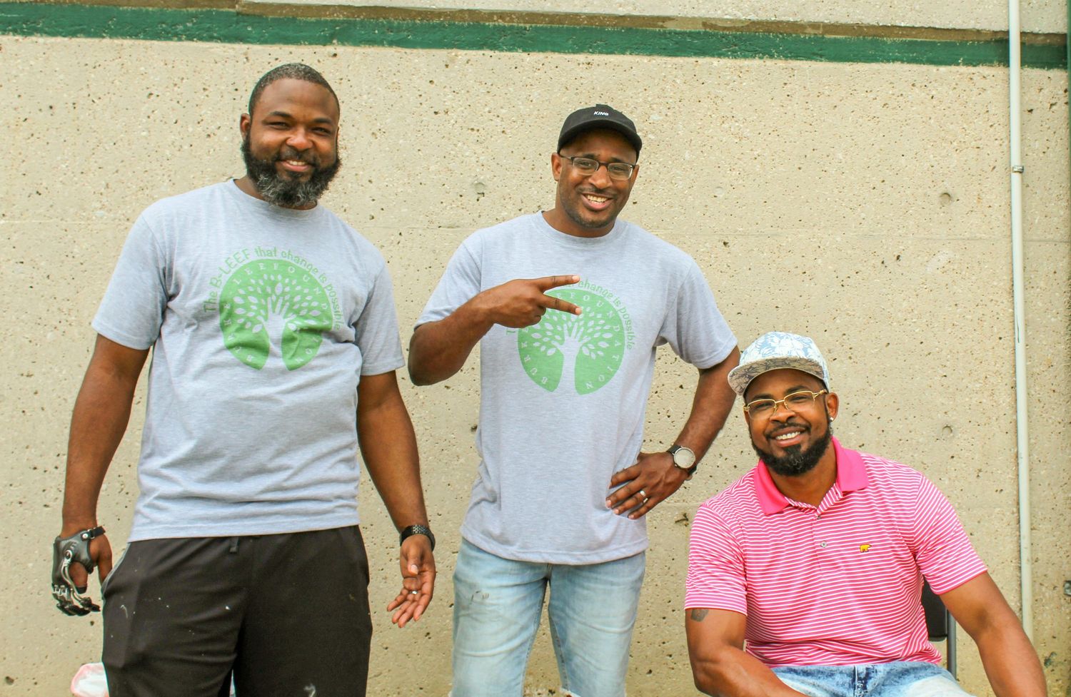 Group of people in casual attire gather outdoors against a beige wall.