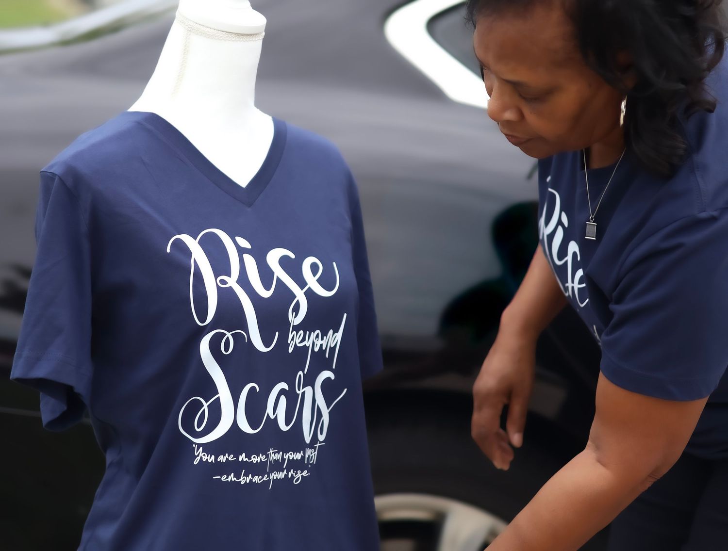 Navy blue t-shirt with 'Rise and Soar' cursive text design being displayed on mannequin form.