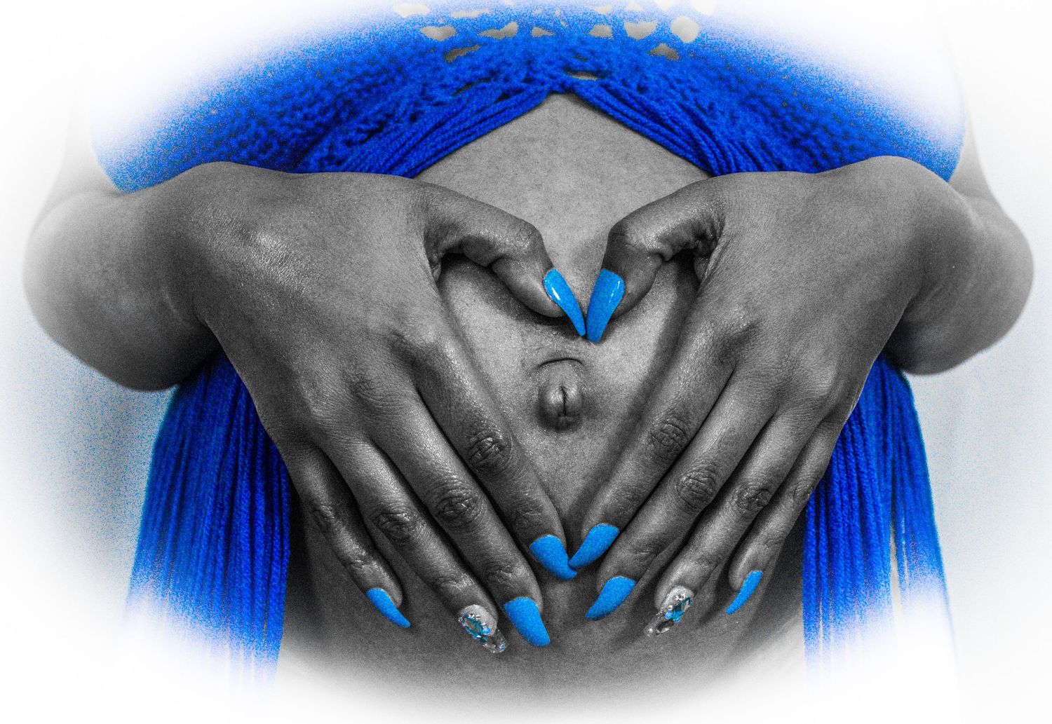 Selective color maternity photo with hands forming heart shape over belly.