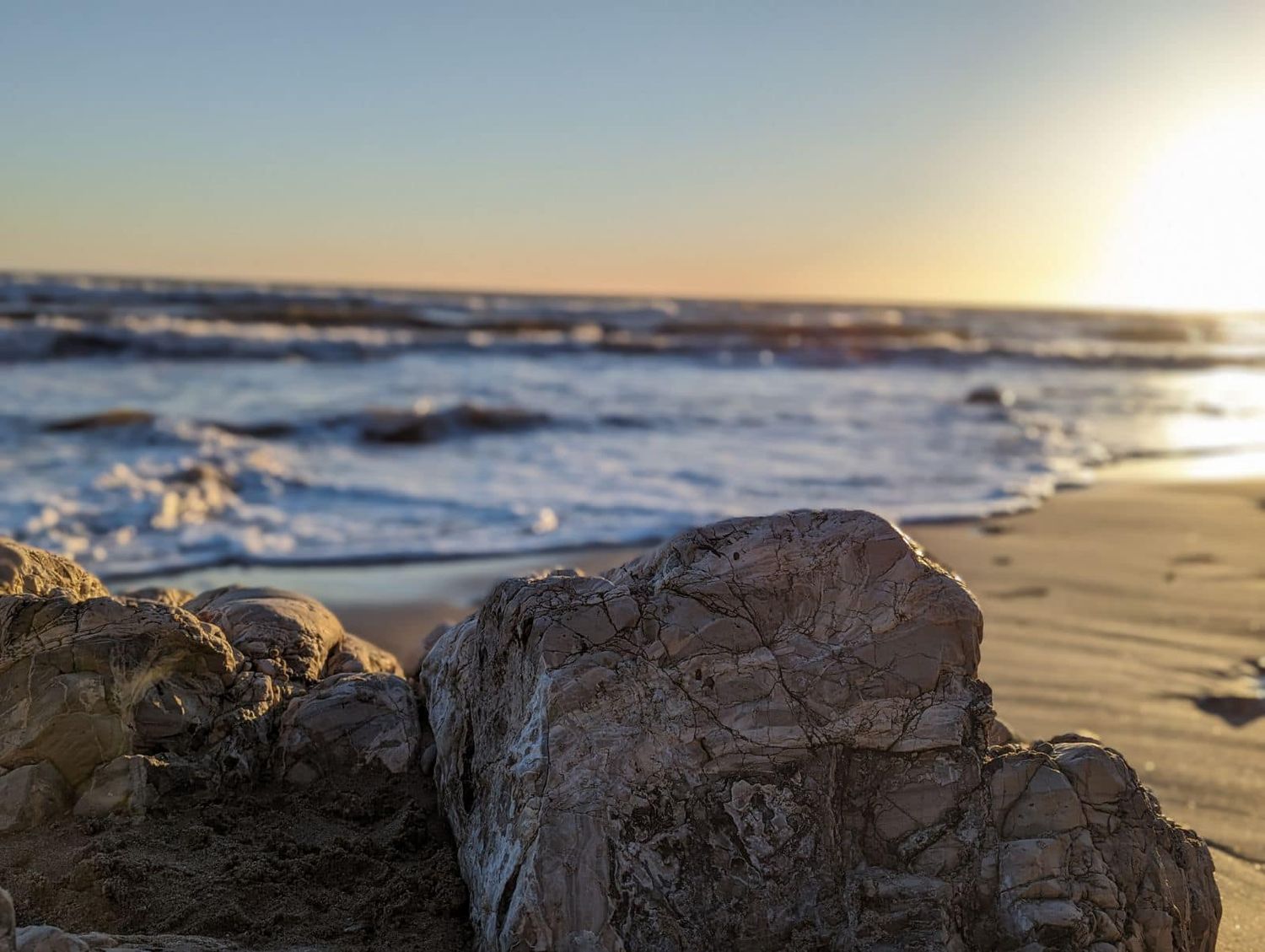 Scenic beach landscape at sunset with waves crashing on rocky shore.