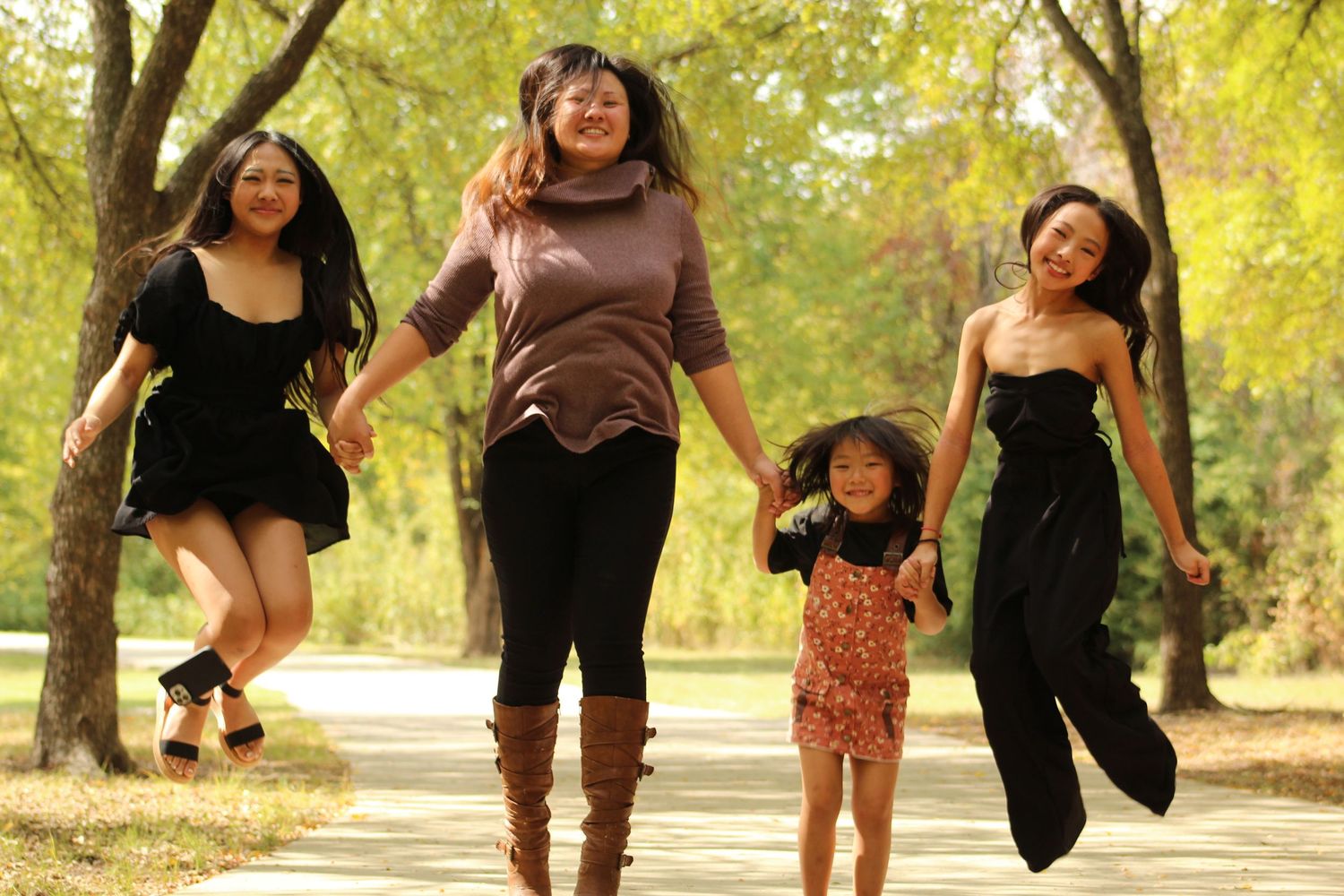 Group of friends jumping playfully on a tree-lined path during an autumn photoshoot.