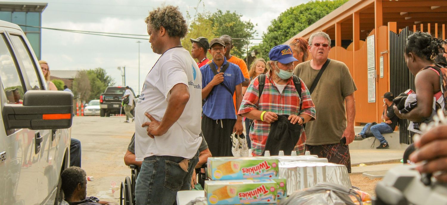 Outdoor gathering with boxes and supplies being distributed on a sunny day.