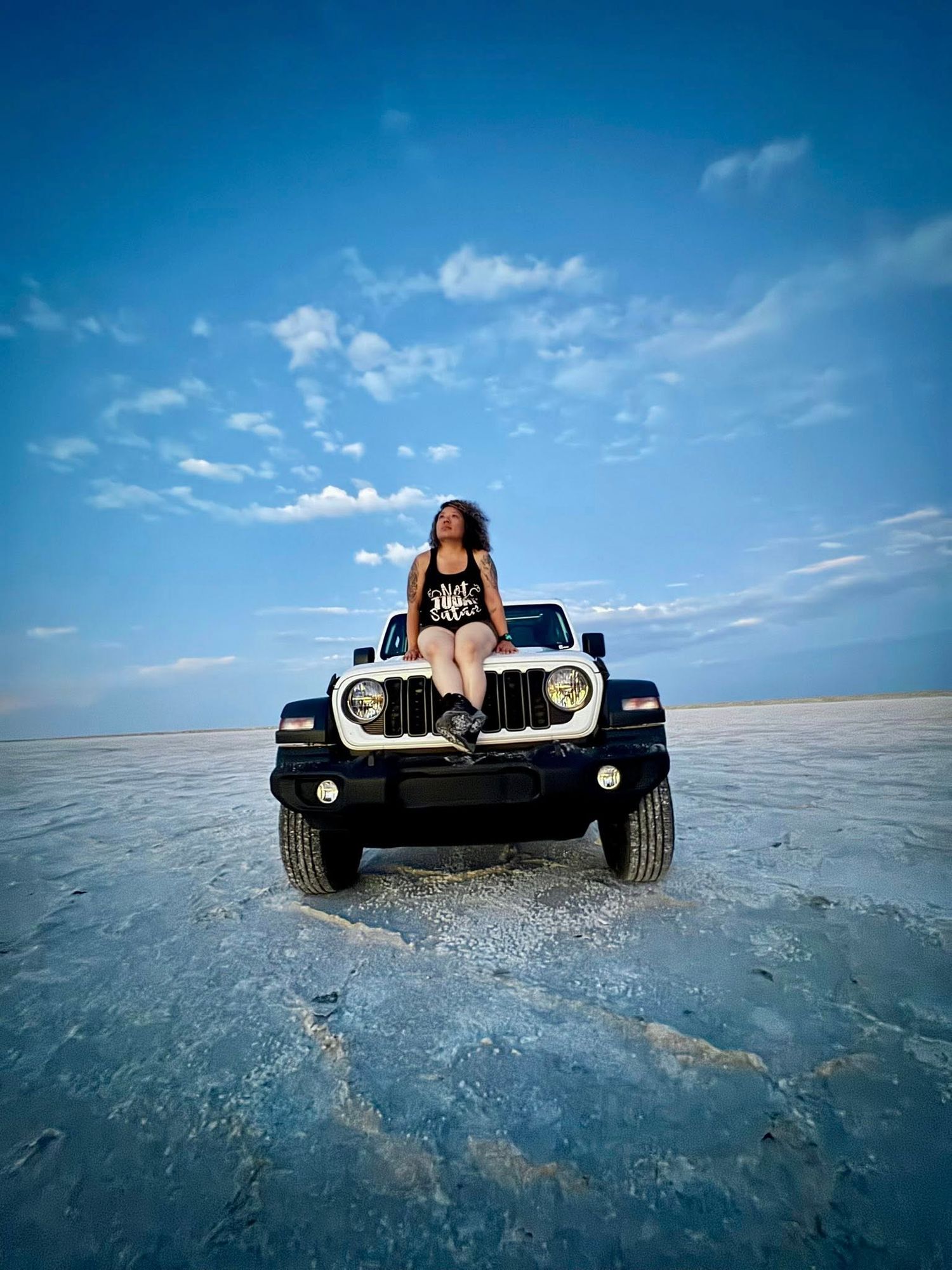 A black dune buggy sits on the reflective surface of a salt flat under a bright blue sky.