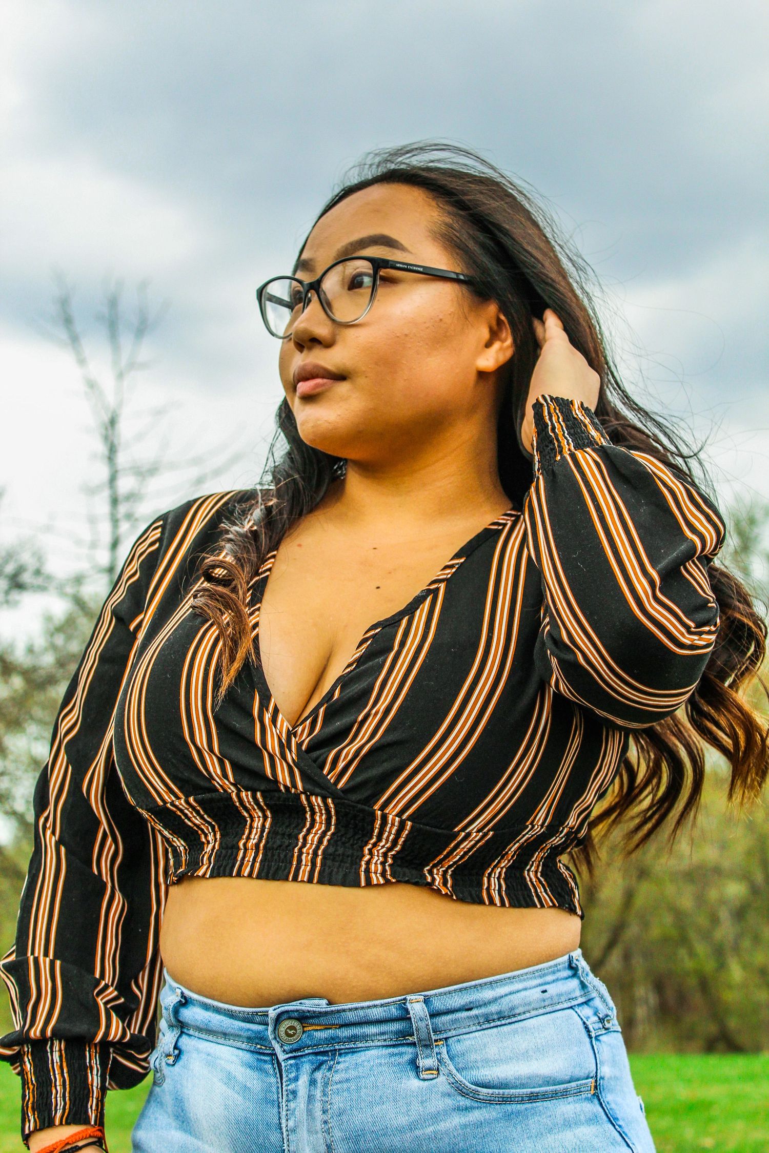 Stylish black and tan striped crop top paired with denim jeans against a cloudy sky backdrop.